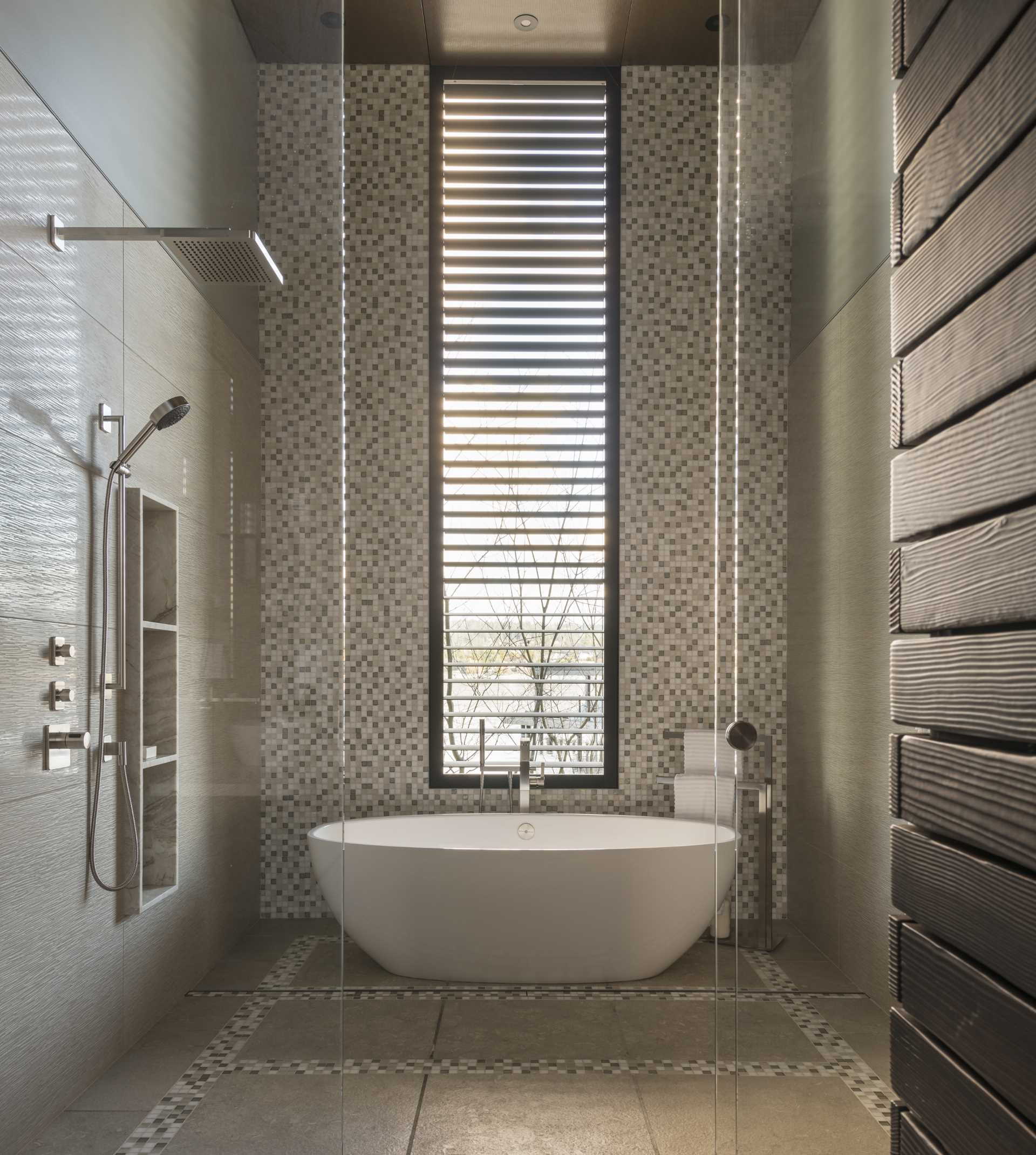 A modern bathroom with a high ceiling, a freestanding bathtub, and a wall of tiles.