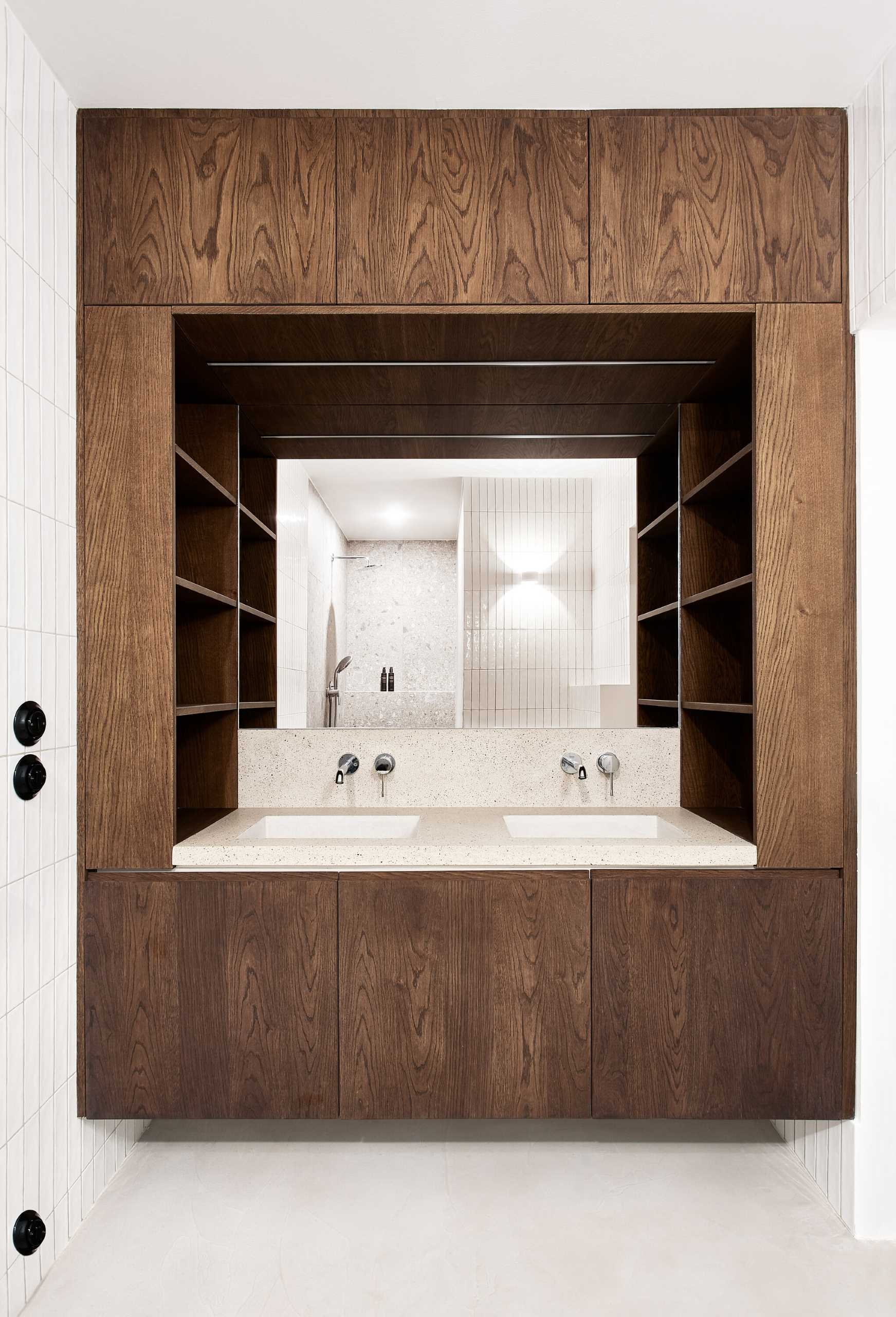 In this modern bathroom, wood cabinetry surrounds the vanity, while a concrete countertop includes built-in sinks, and white tiles line the wall.