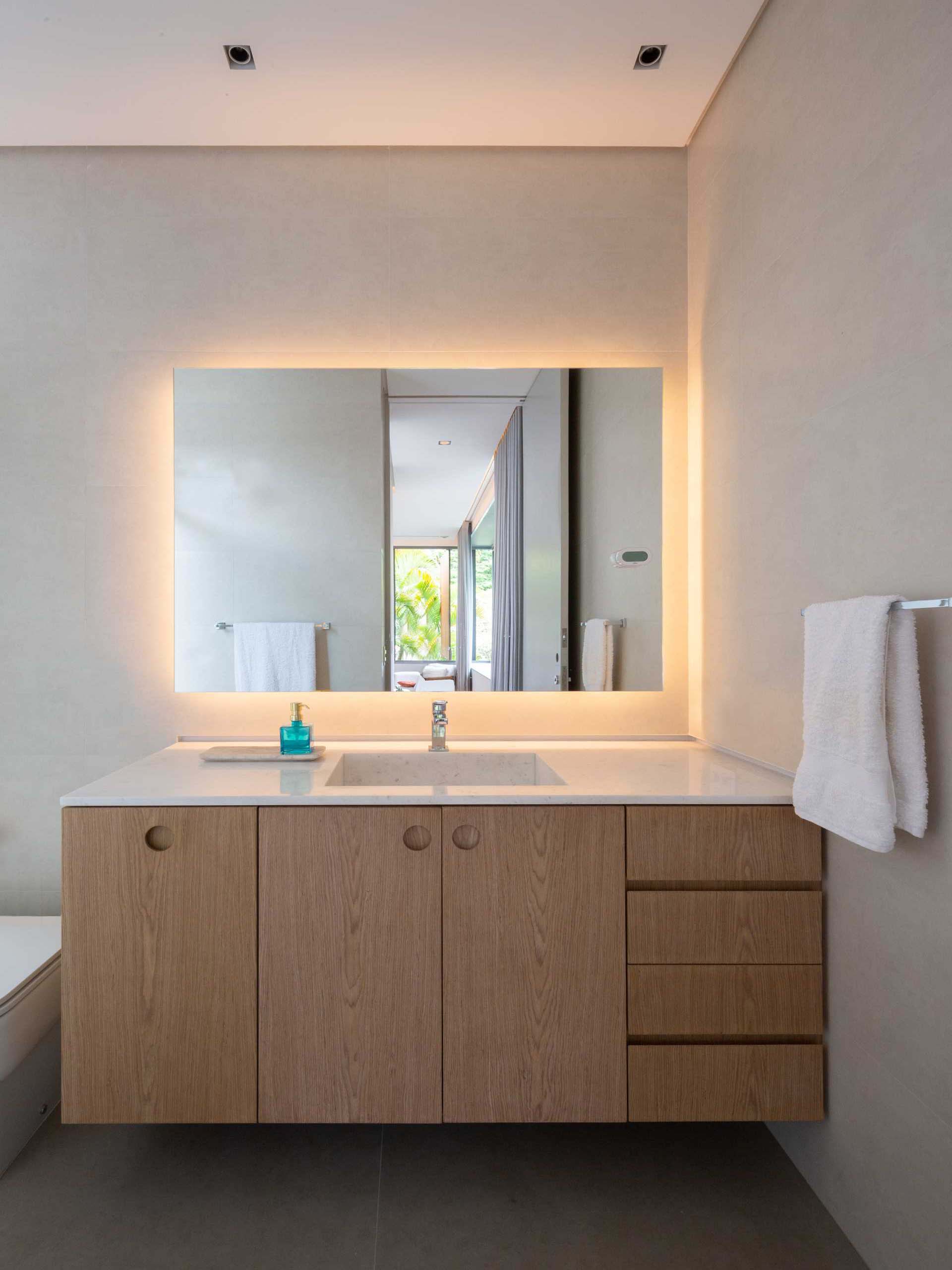 In this modern bathroom, there's a wood vanity with a backlit mirror above.