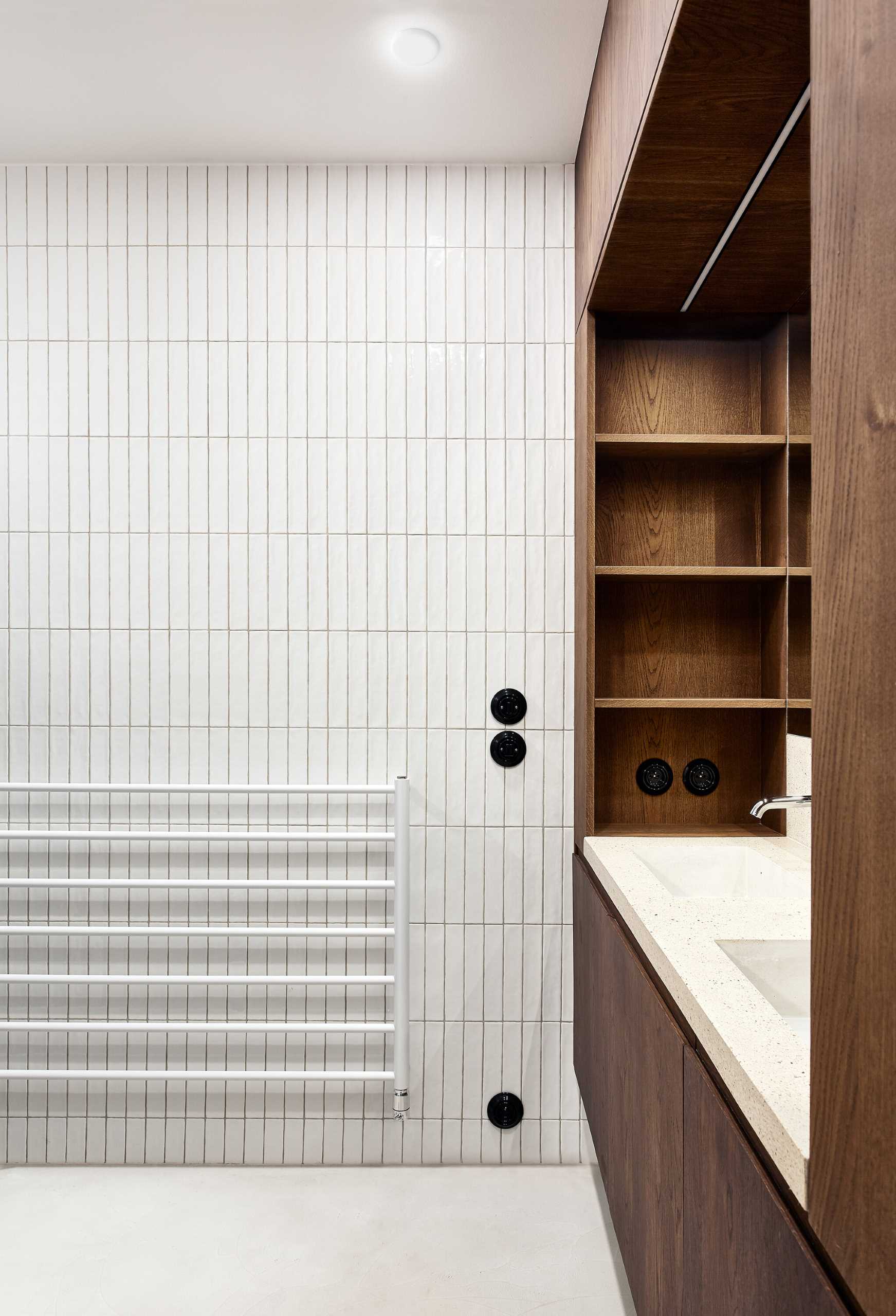 In this modern bathroom, wood cabinetry surrounds the vanity, while a concrete countertop includes built-in sinks, and white tiles line the wall.