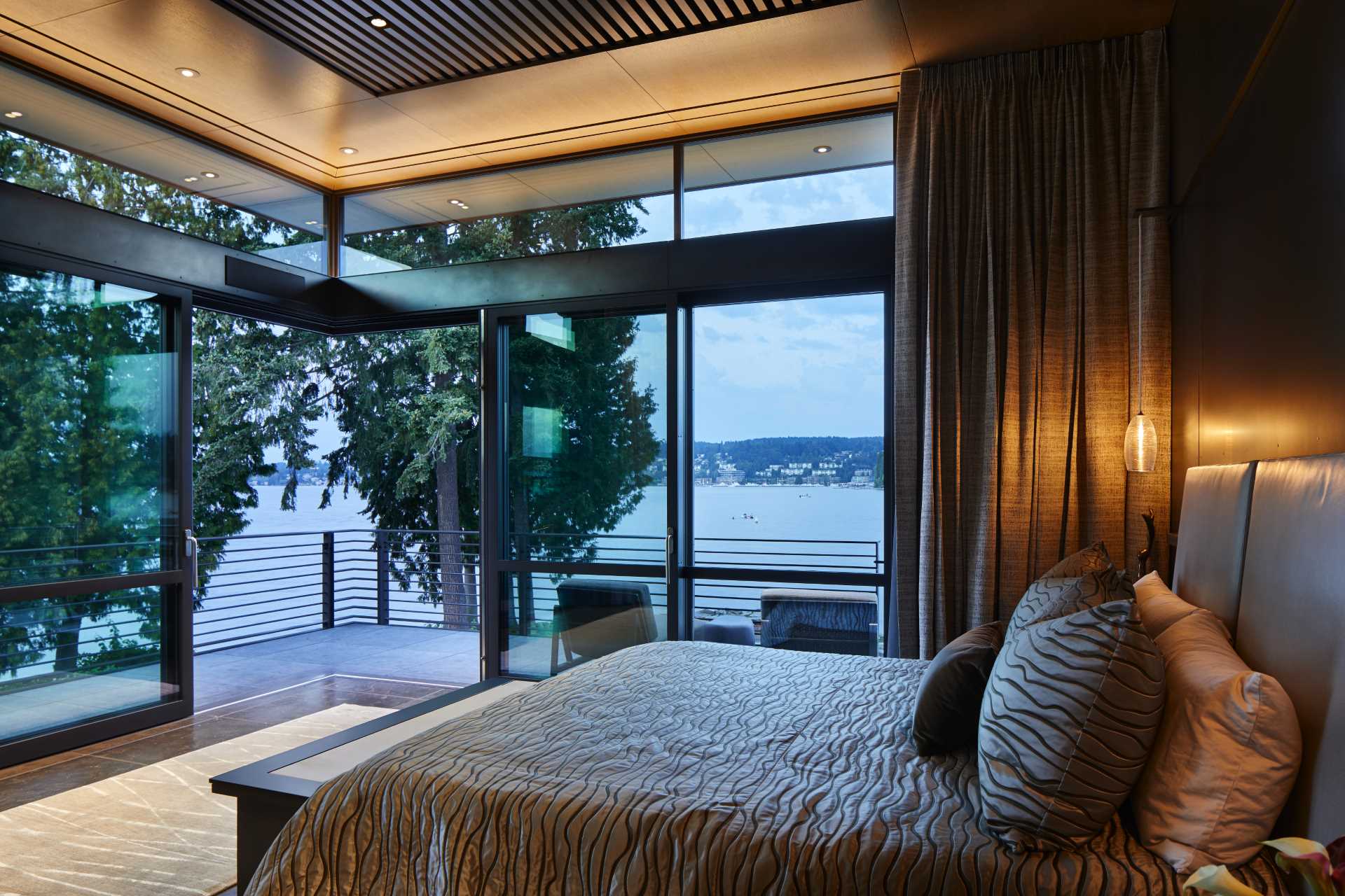 A modern bedroom with glass walls that open to a balcony.