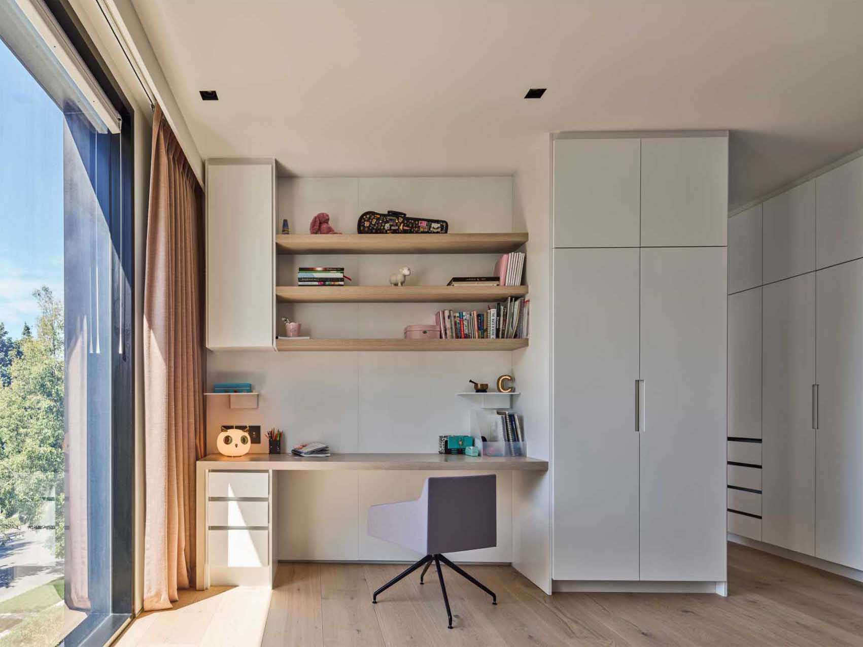 A modern bedroom with a built-in study desk and floating shelves.