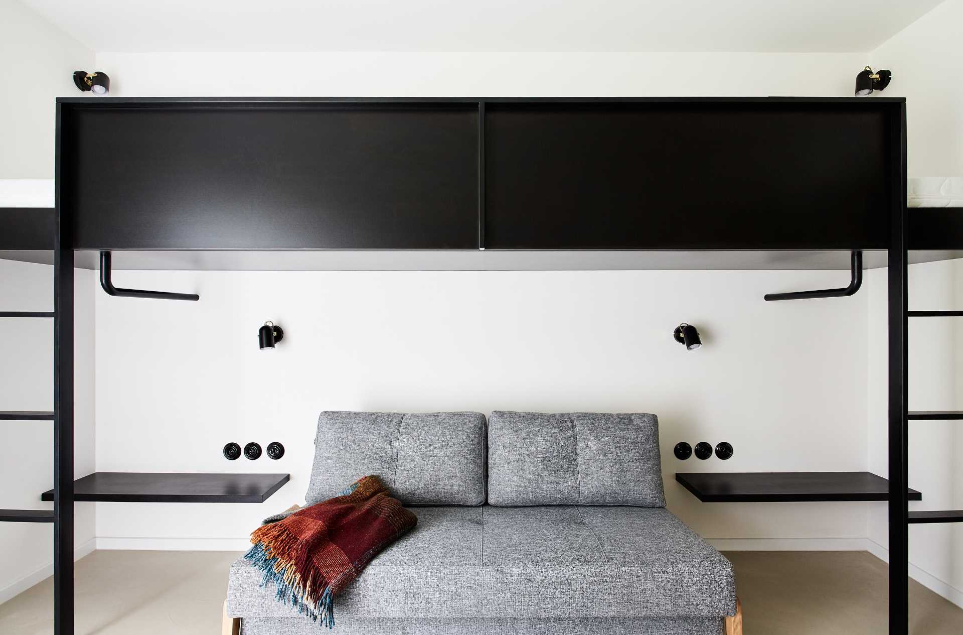 This modern bedroom includes two loft beds in a black frame. Underneath, there's a comfortable couch with two side tables. The couch can also be transformed into an additional bed.