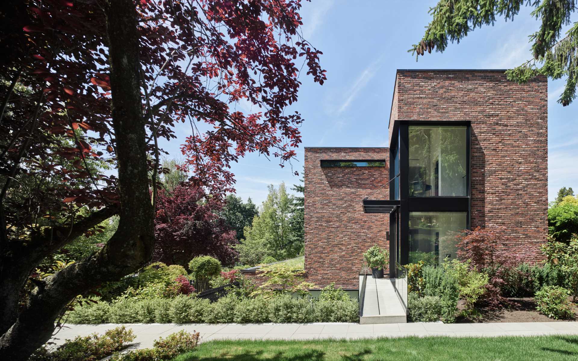 The front door of this modern brick house is accessed across a long steel bridge that floats above a sunken patio.