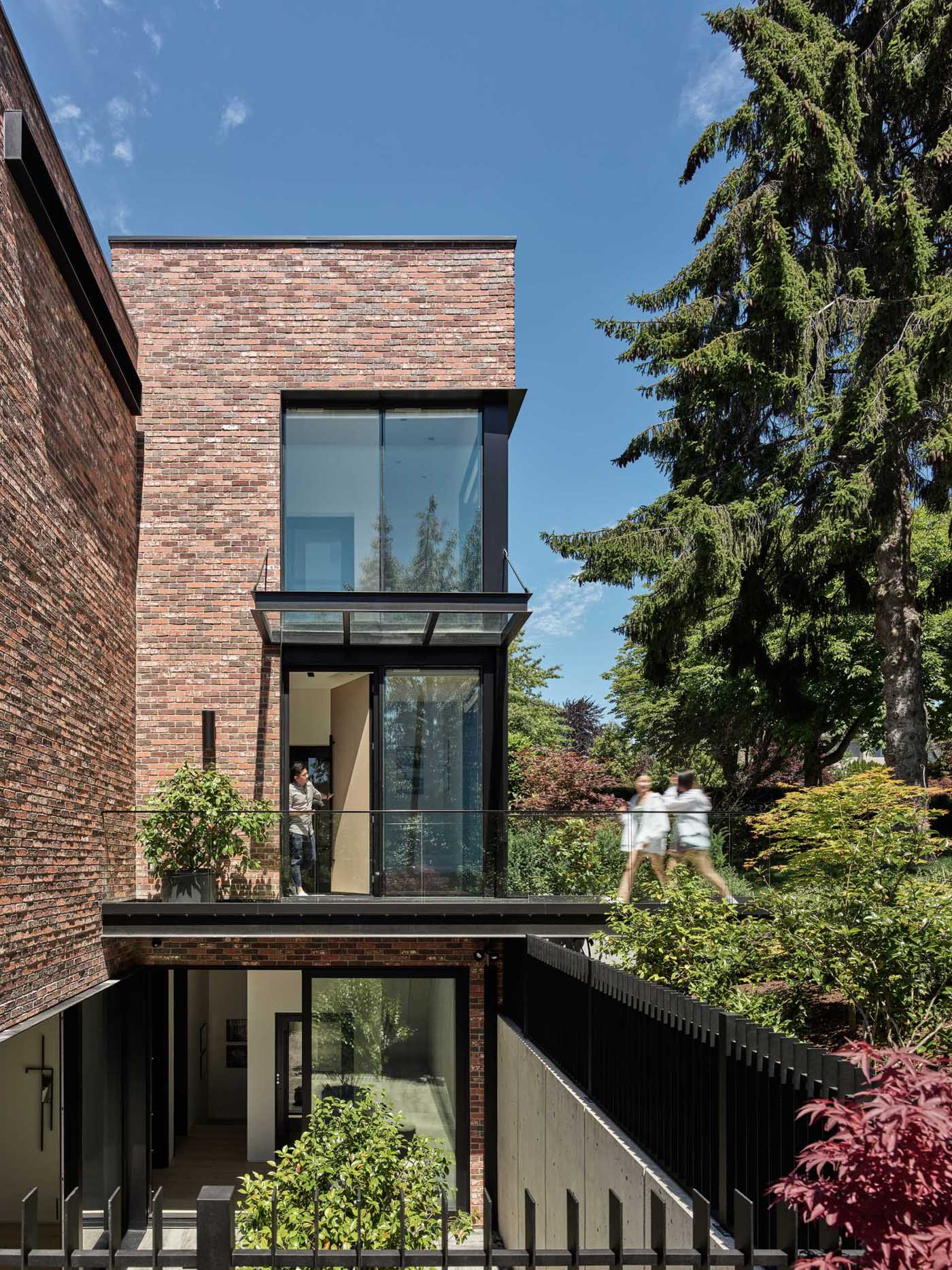 The front door of this modern brick house is accessed across a long steel bridge that floats above a sunken patio.