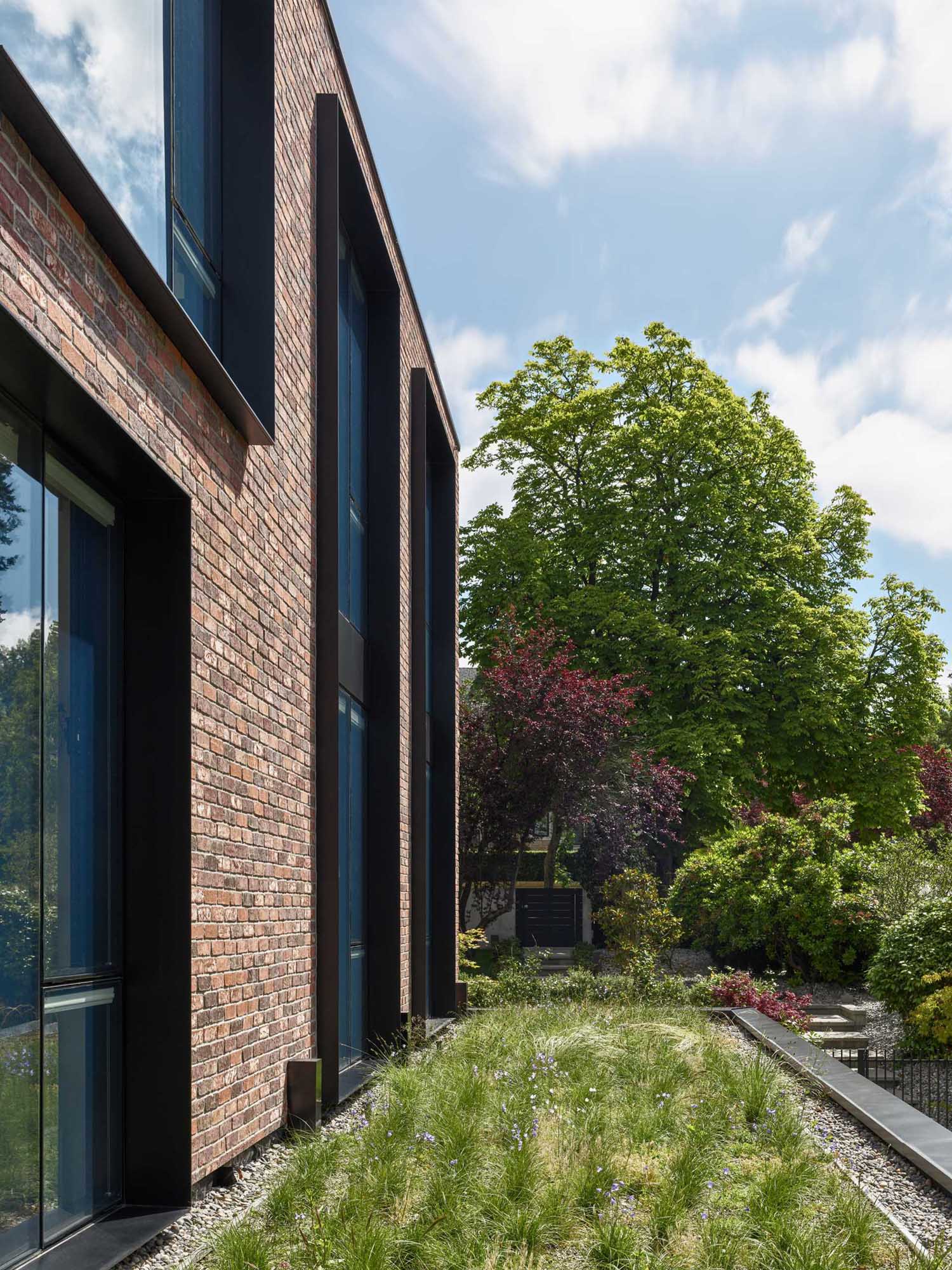 A modern brick house with black steel window frames and a green roof.