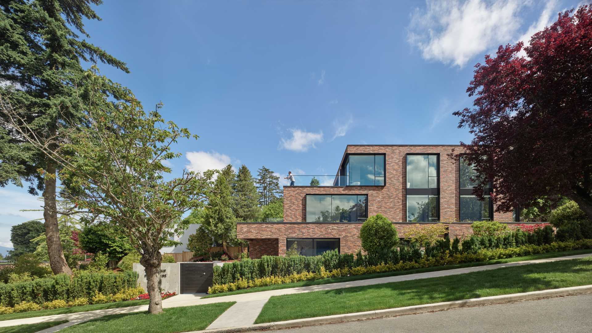 A modern brick house with a staggered design, has black window frames and glass railings.