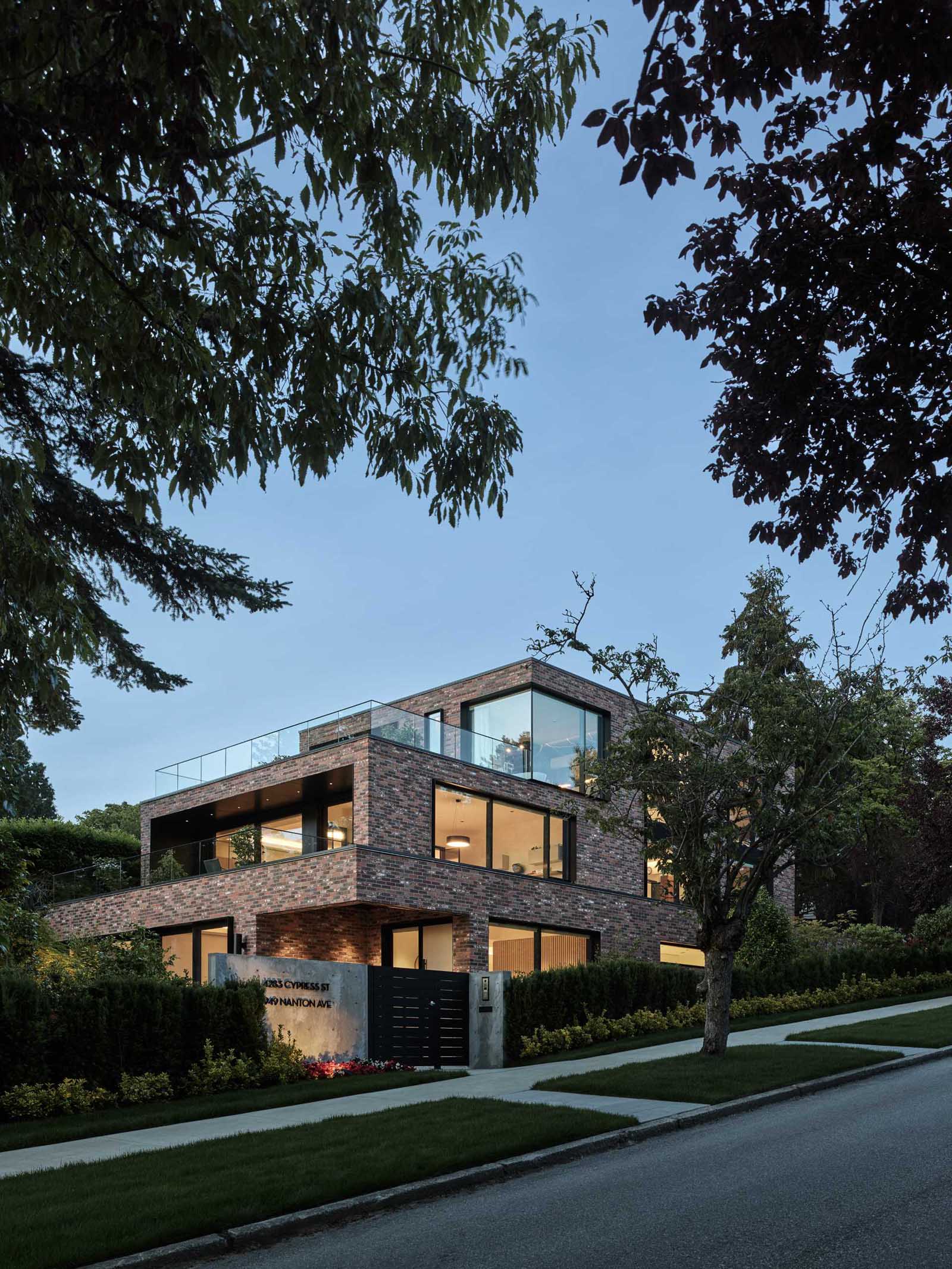 A modern brick house with a staggered design, has black window frames and glass railings.