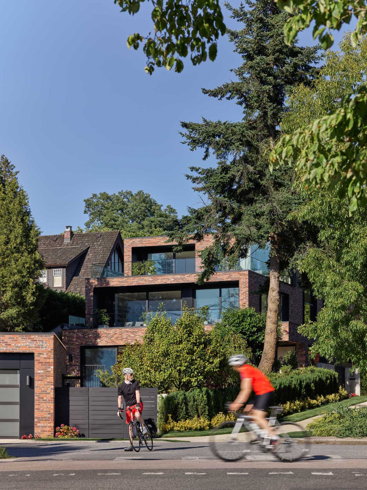 A modern brick house with a staggered design, has black window frames and glass railings.