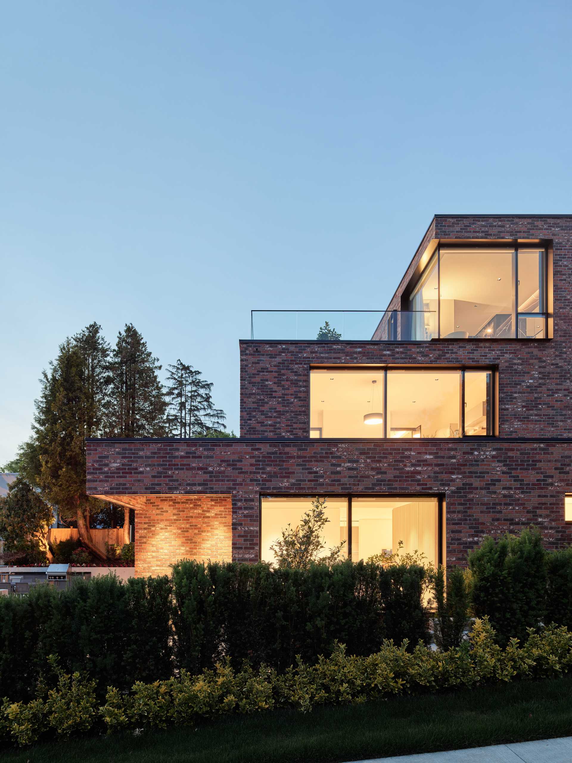 A modern brick house with a staggered design, has black window frames and glass railings.