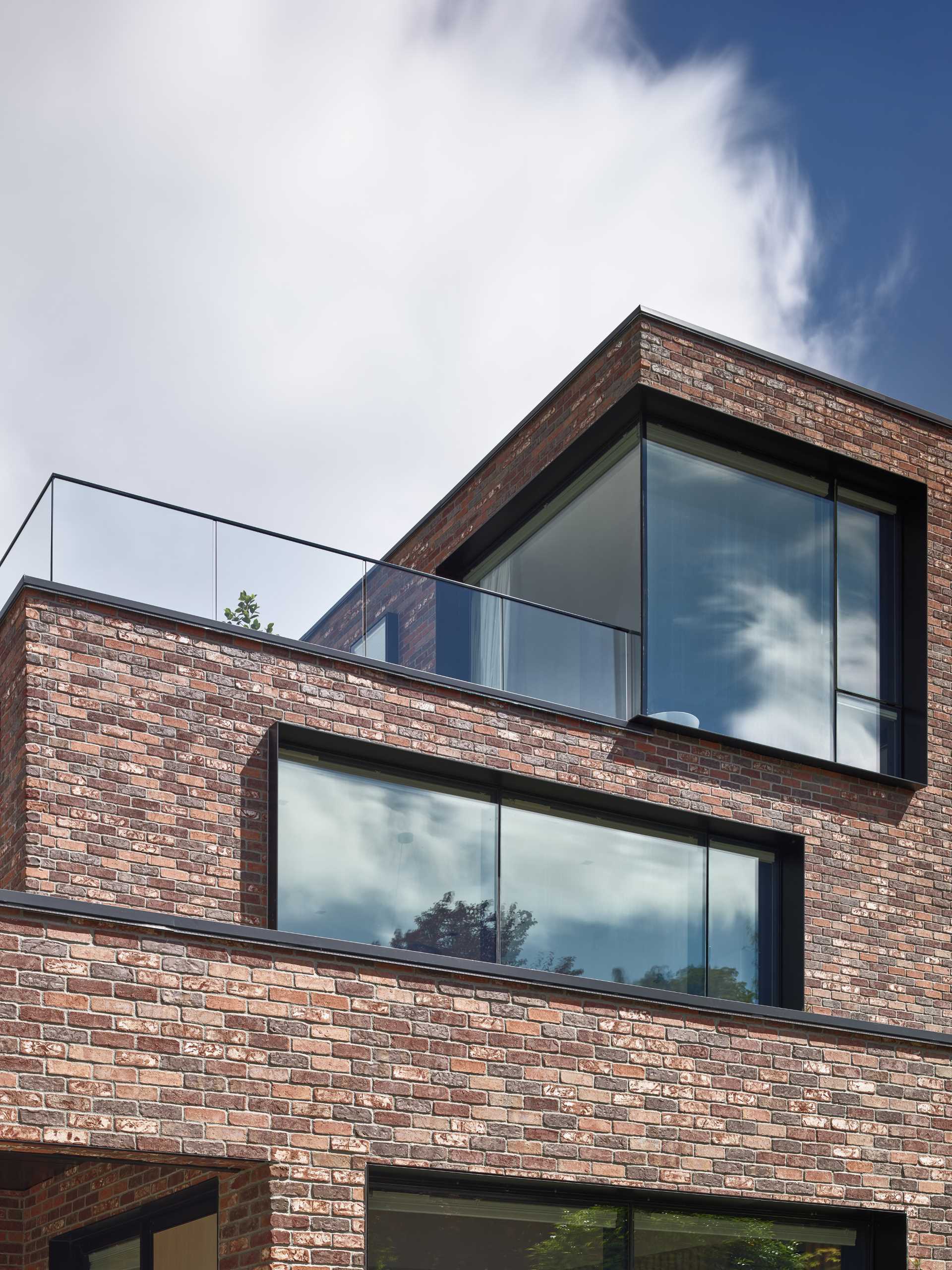A modern brick house with black window frames and glass railings.