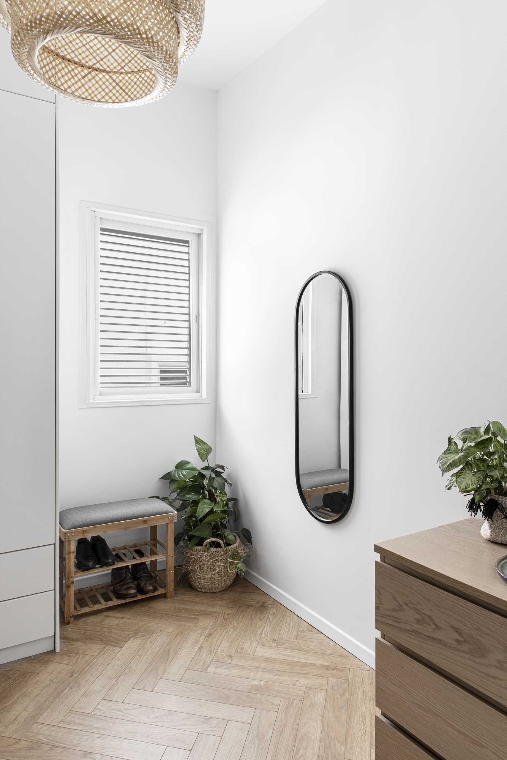 In this modern bedroom, there's a corner with a bench, a plant, a mirror, and a dresser.