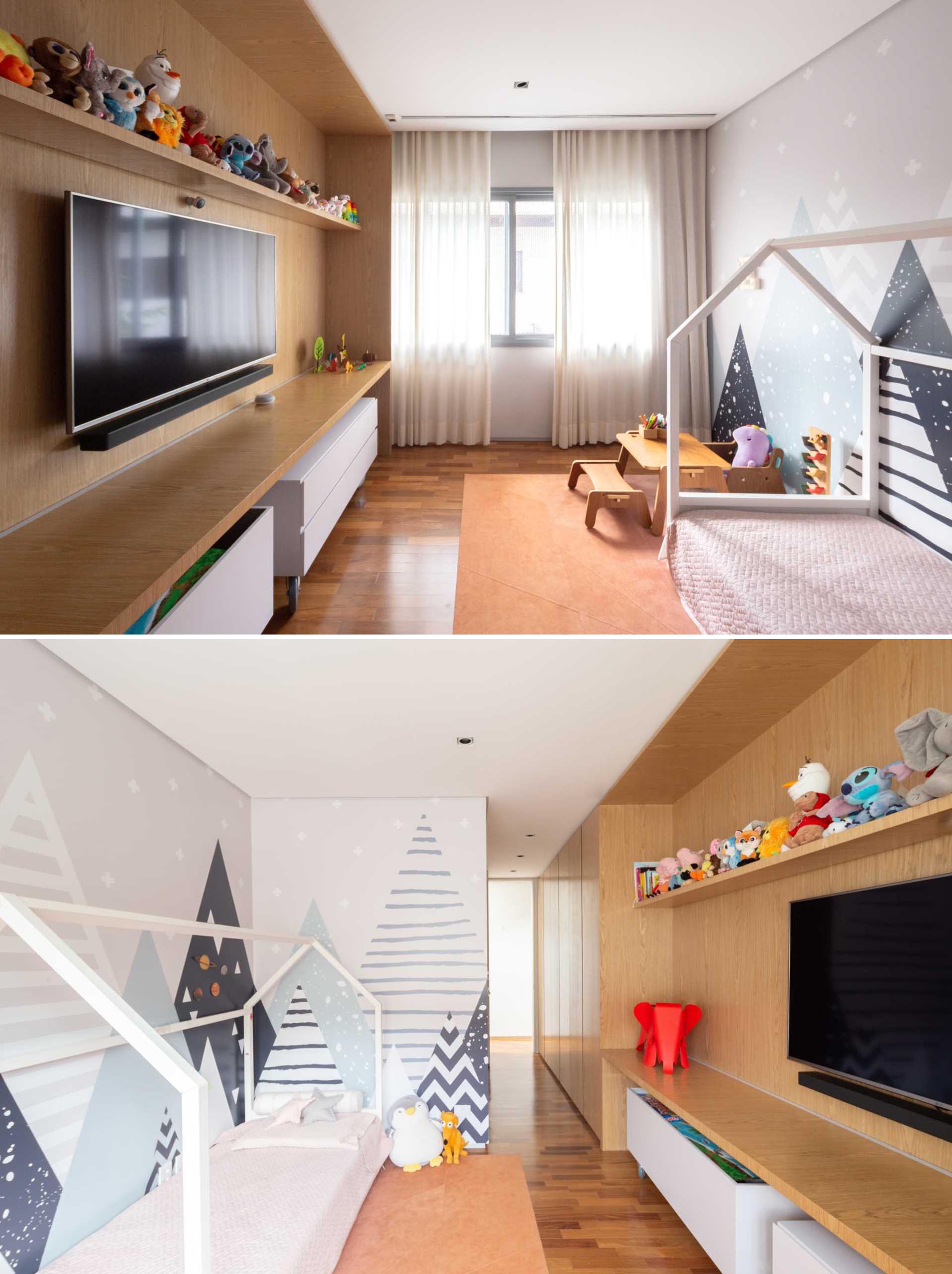 This kids bedroom includes a graphic mountain wall mural, while the opposite wall has a wood feature with a shelf for toys, a TV, and room for additional storage underneath.