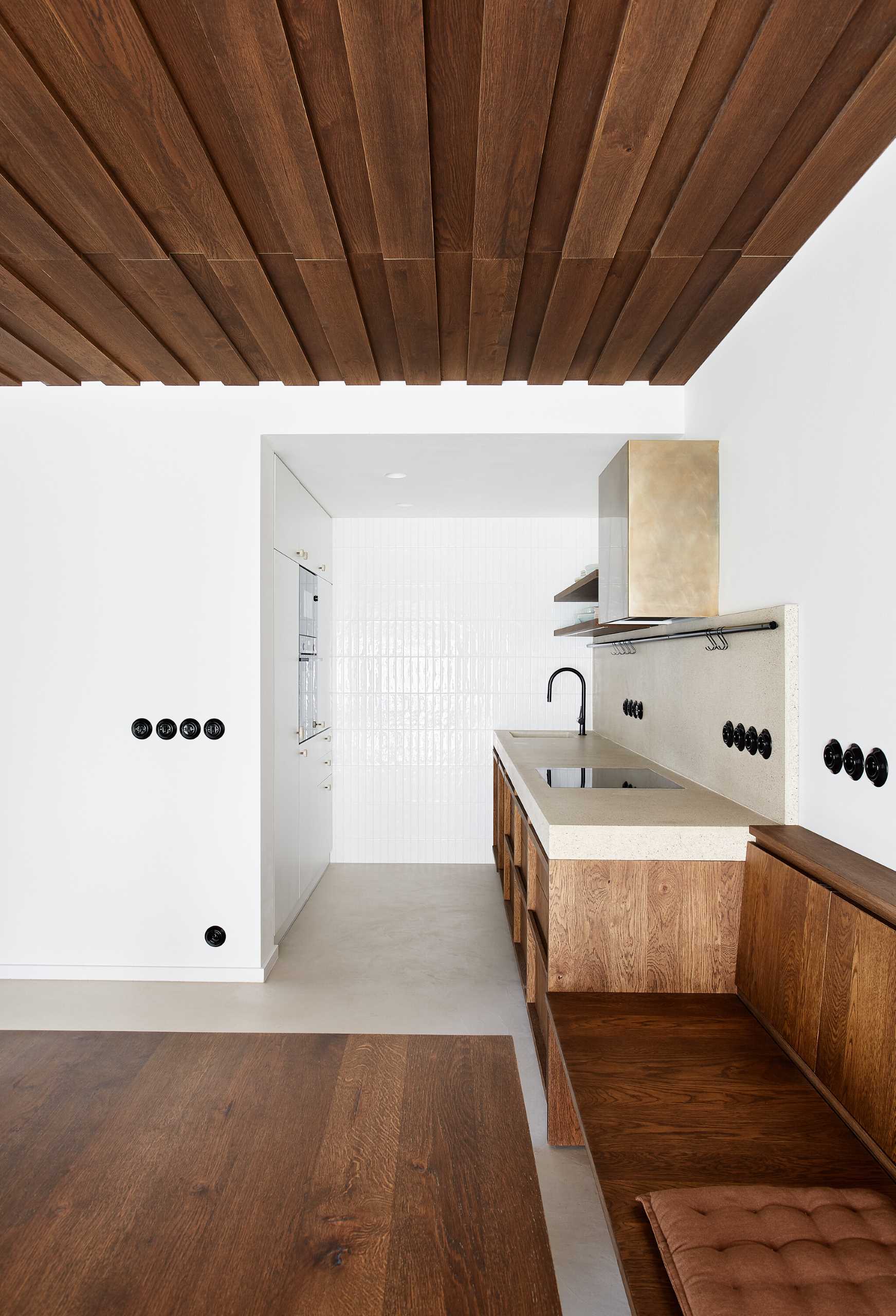 This modern kitchen has a wall of white tiles, a concrete countertop, and wood cabinets.