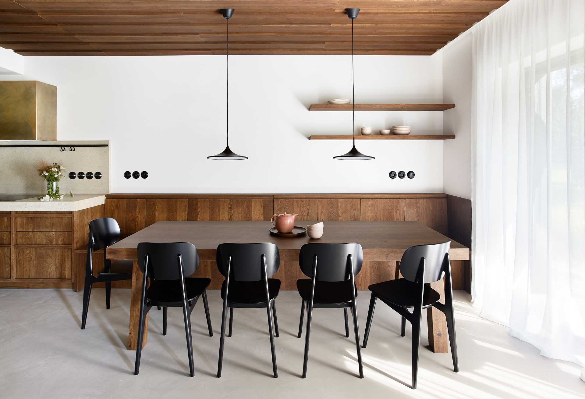 A modern open plan dining area includes a built-in wood banquette that creates plenty of seating for the owners and their guests when they are visiting on holiday.