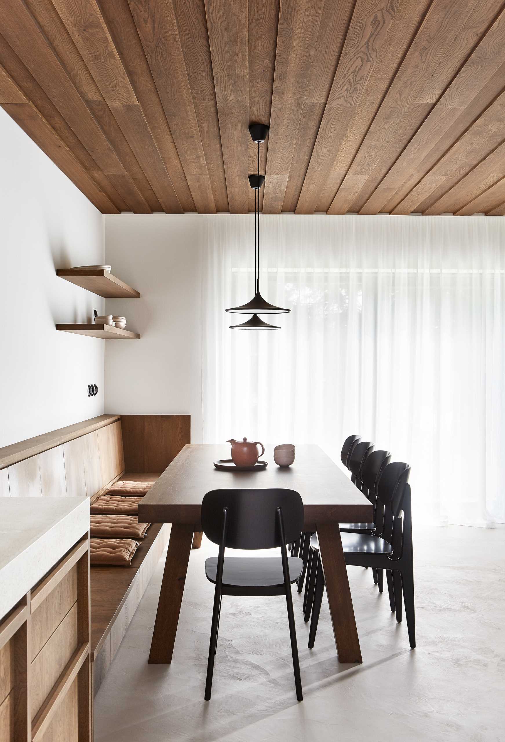 A modern open plan dining area includes a built-in wood banquette that creates plenty of seating for the owners and their guests when they are visiting on holiday.