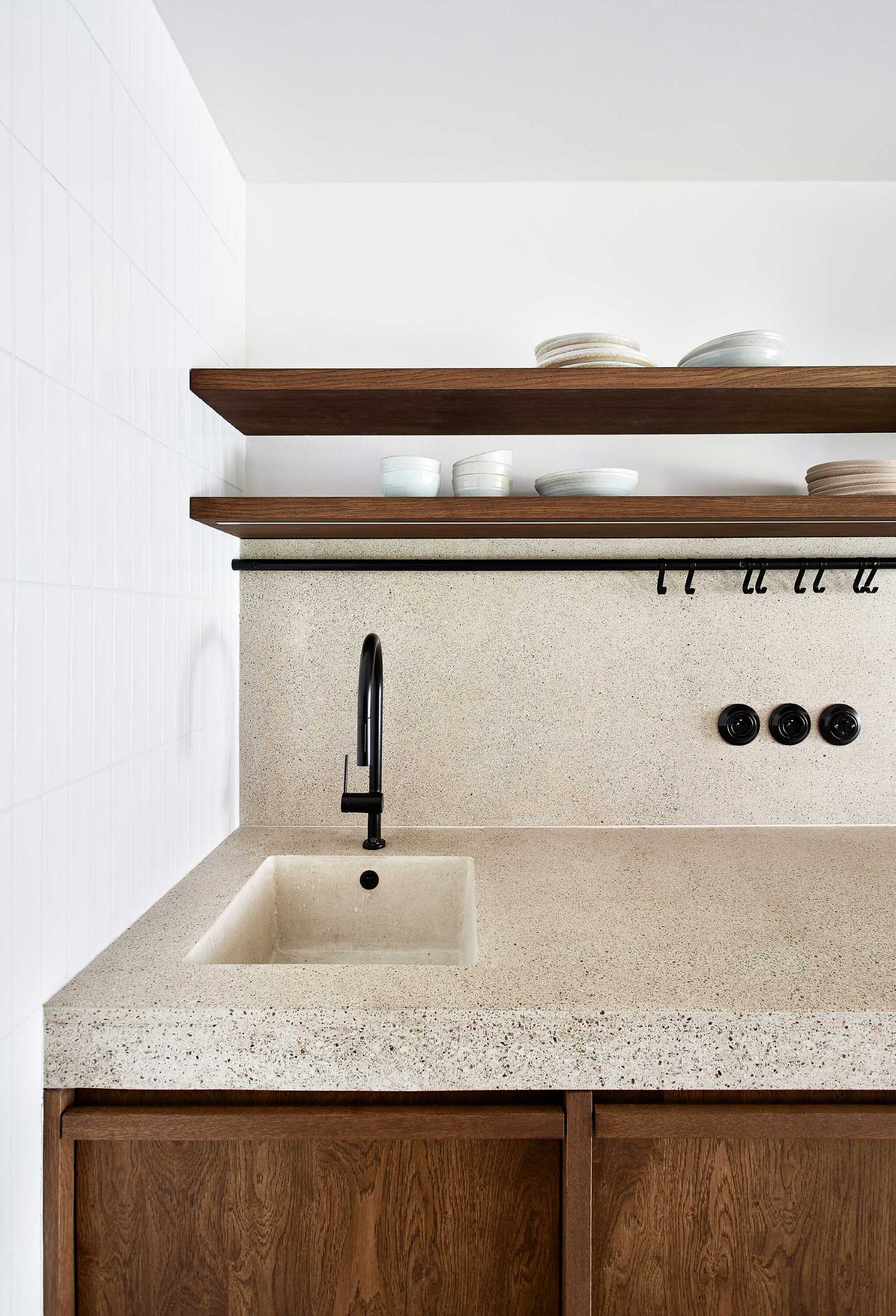 This modern kitchen has a wall of white tiles, a concrete countertop, and wood cabinets.