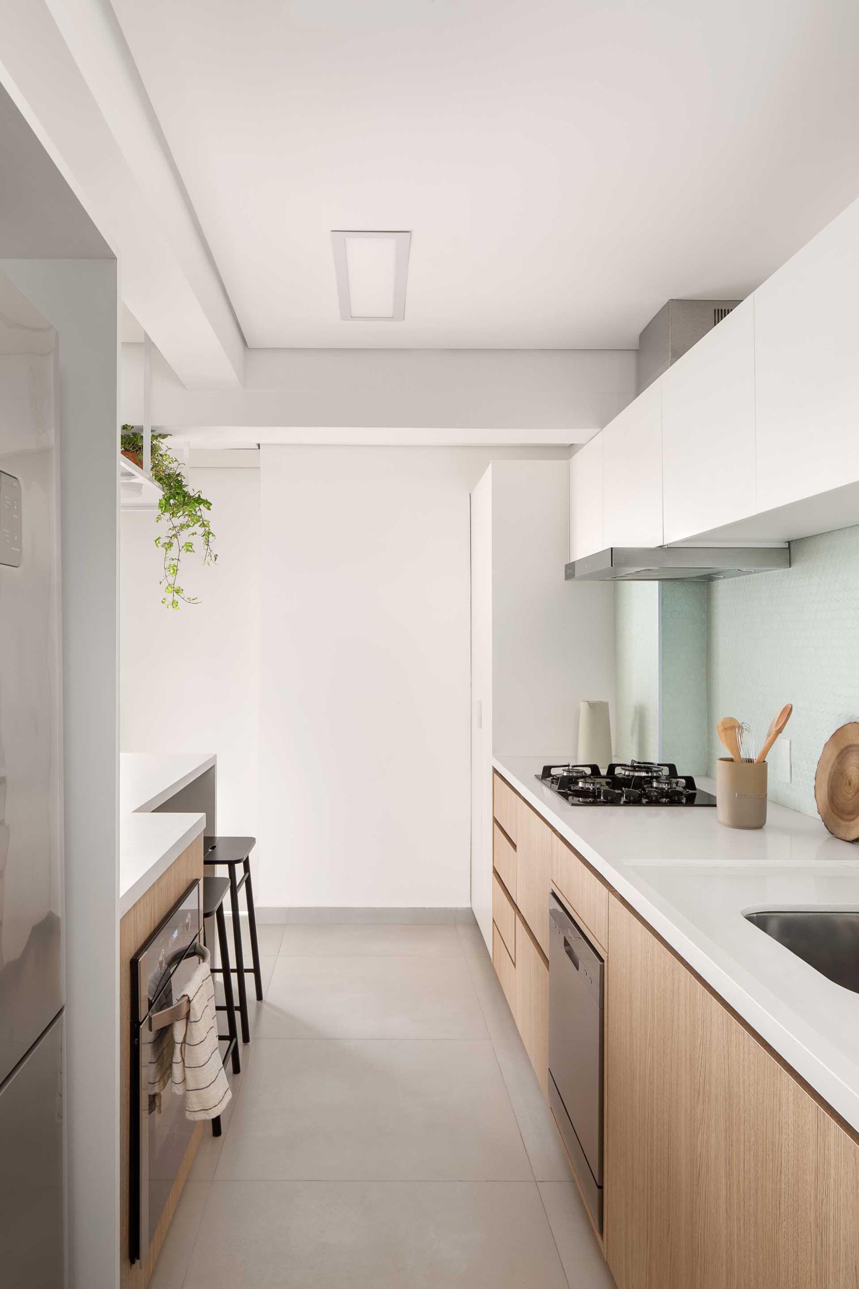 In this modern kitchen, minimalist wood cabinets have been paired with white countertops and upper cabinets, and a light green backsplash.