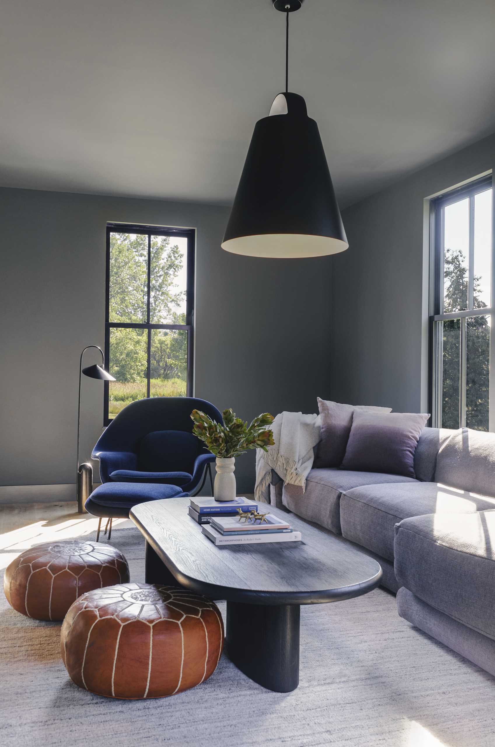 A modern TV room finished with dark grey walls, comfortable furniture, and a large black pendant light.