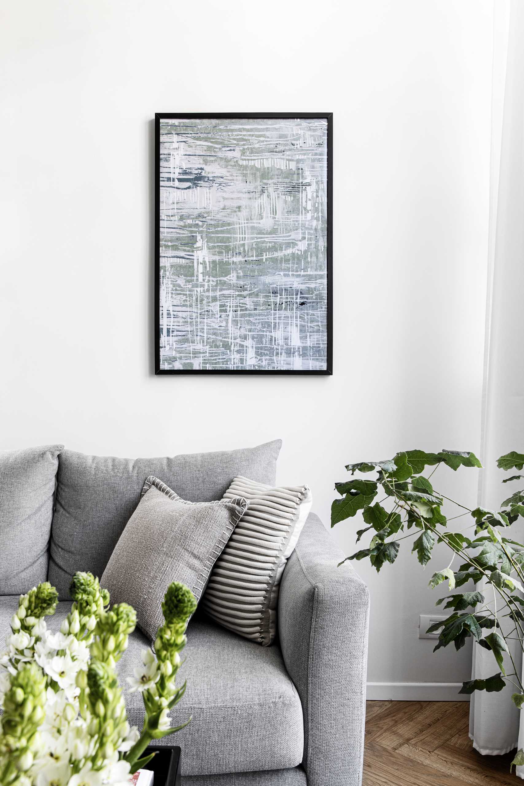 Uma moderna sala de estar com paredes claras, um sofá cinza e plantas.