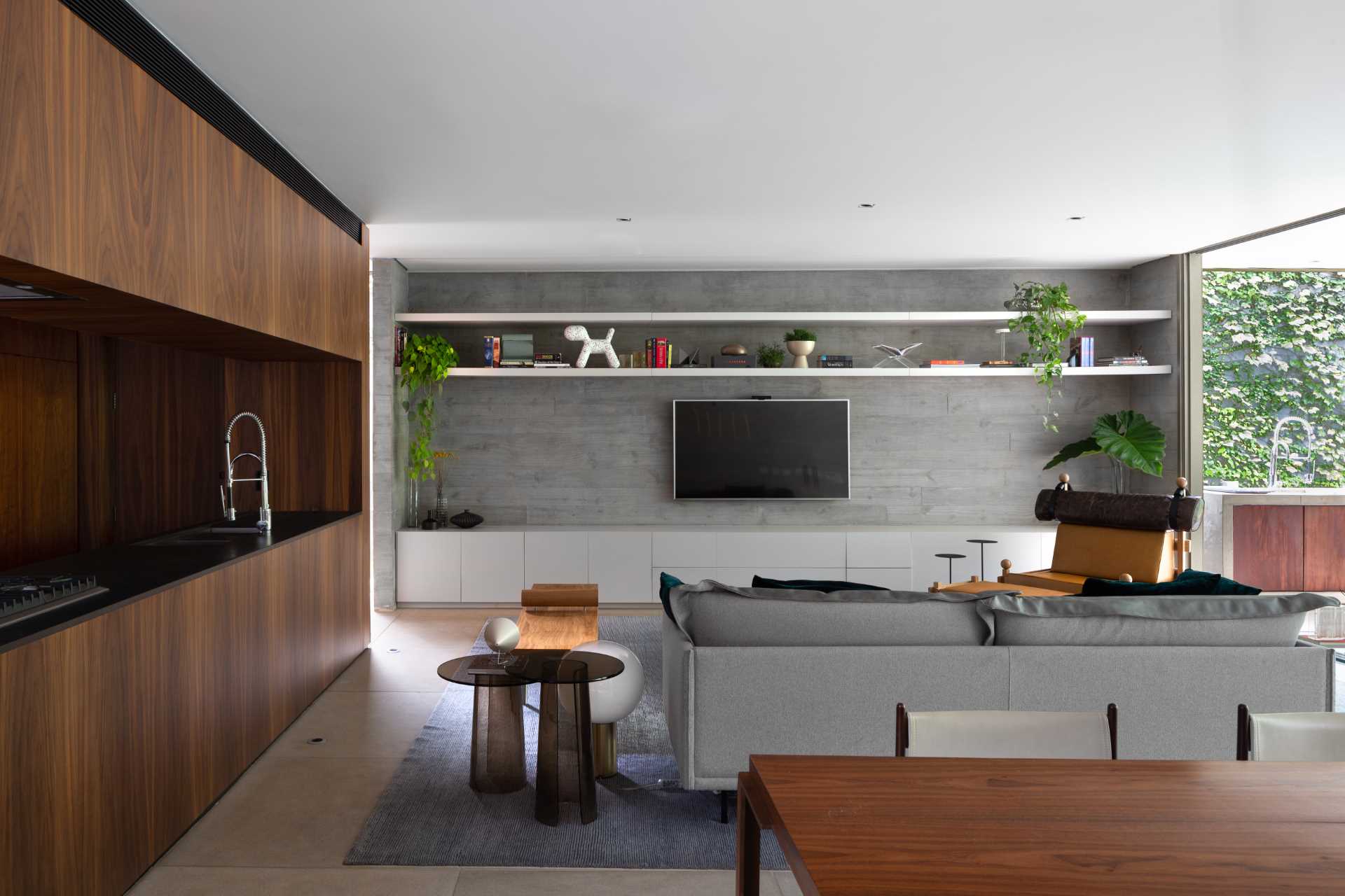 The furniture in this modern living room faces a concrete wall that been designed with a row of cabinetry below the TV and two shelves above.