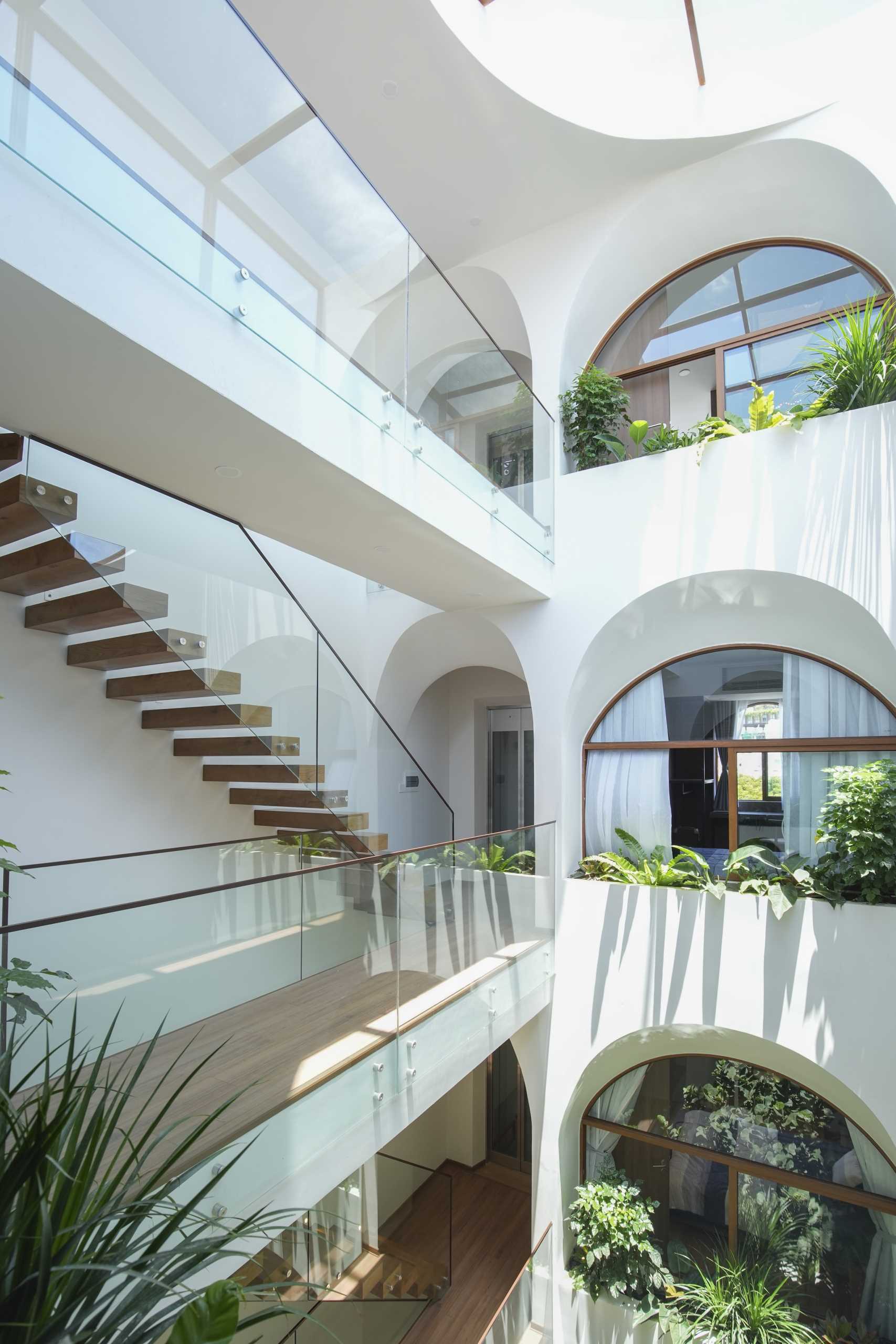 A modern home with an atrium, wood stairs with glass railings, arched openings, and interior bridges.