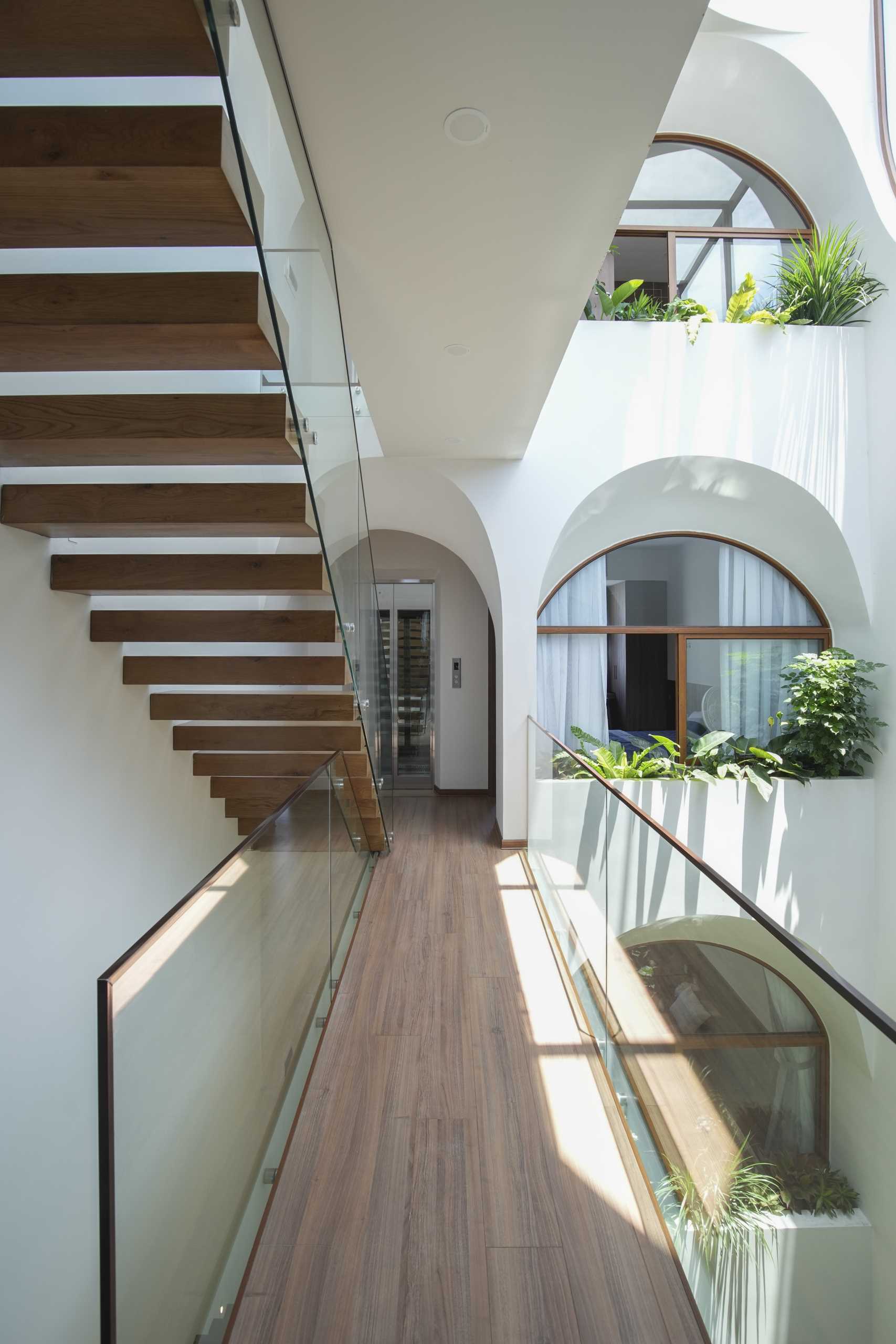 A modern home with an atrium, wood stairs, arched openings, and interior bridges.