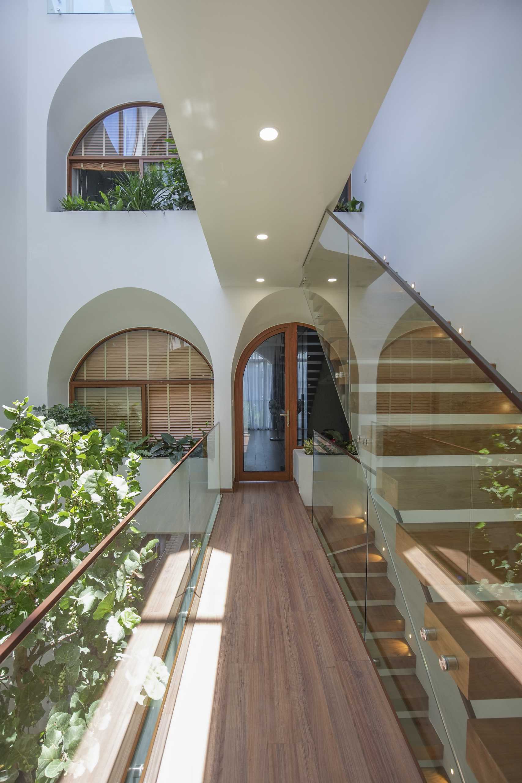 A modern home with an atrium, wood stairs, arched openings, and interior bridges.