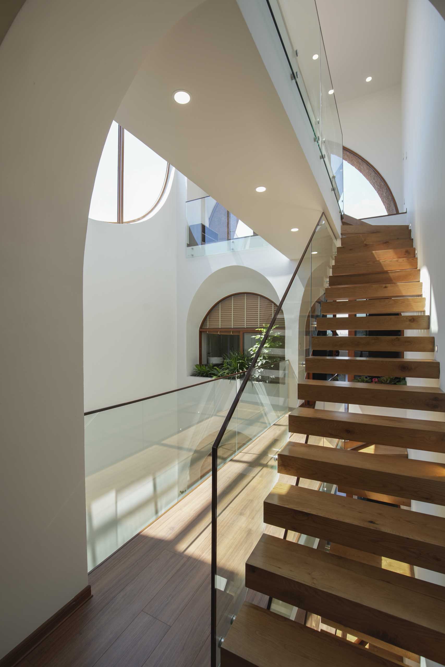 A modern home with an atrium, wood stairs, arched openings, and interior bridges.