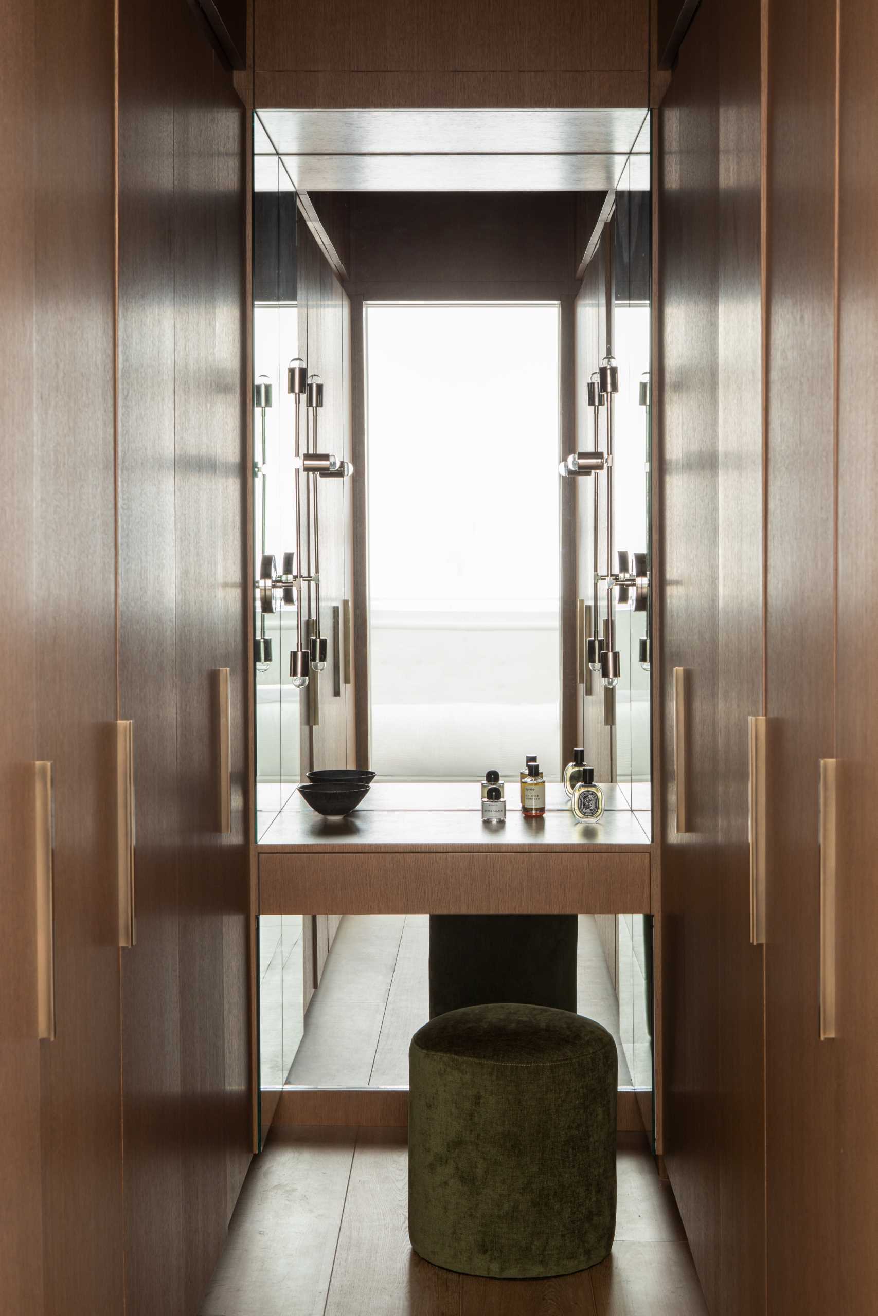 A door in the bedroom opens to reveal a walnut-lined dressing room with warm lighting and infinity mirrors.