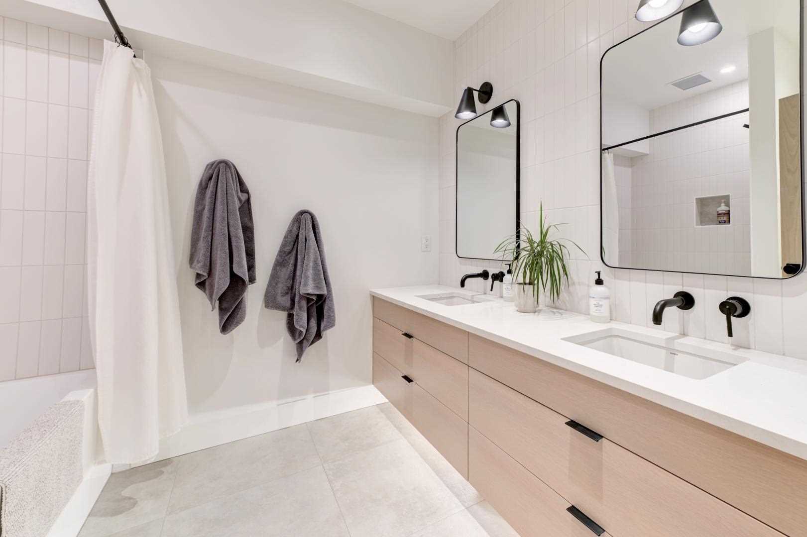This modern bathroom includes a double vanity, while the black framed mirrors complement the black faucets, lighting, drawer pulls, and shower curtain rod.