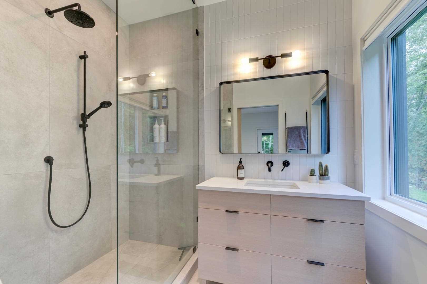 This ensuite bathroom includes white tile wall behind the vanity, and a walk-in shower with a glass screen.