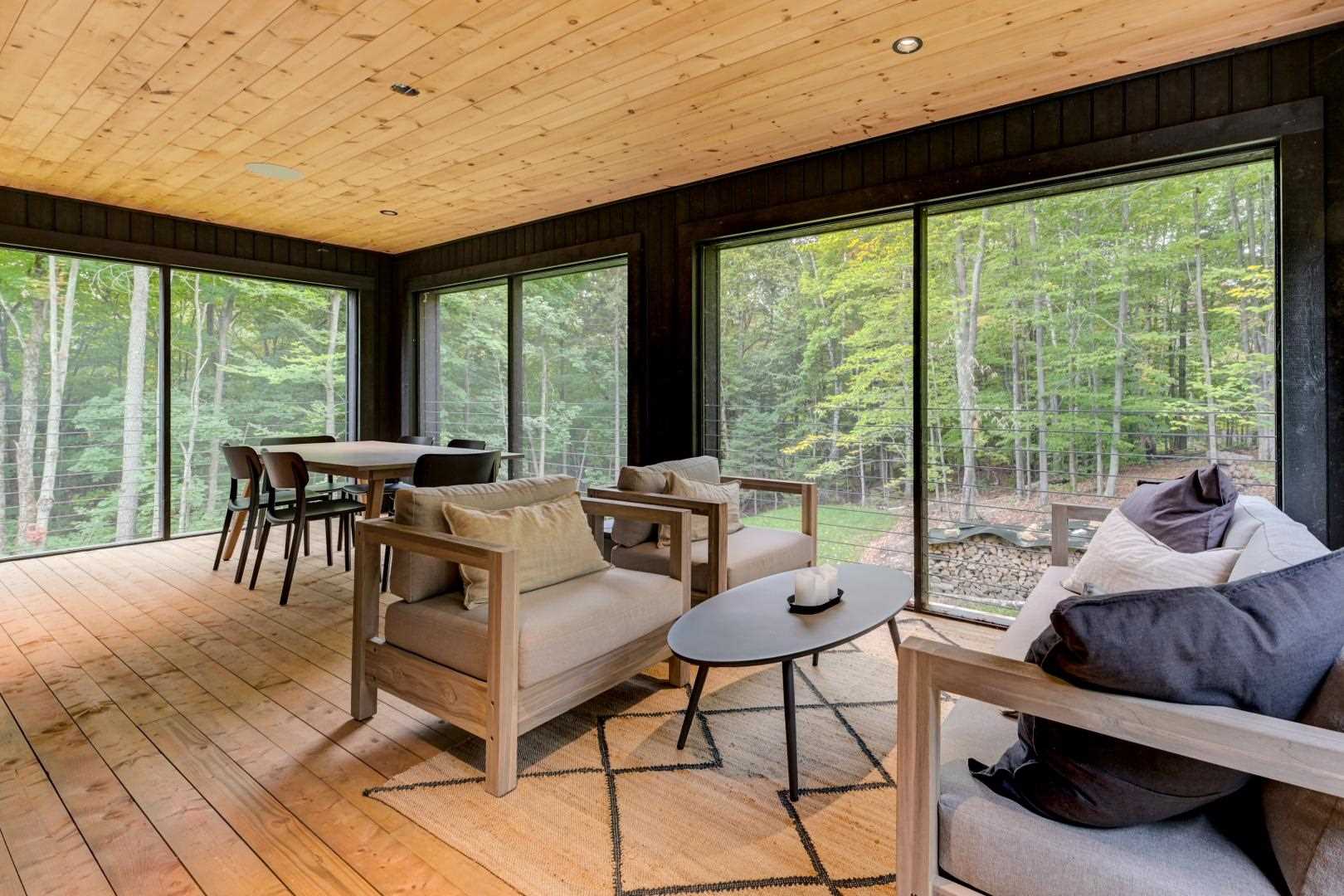 A sunroom with large windows and a wood ceiling, as well as a dining area and lounge.