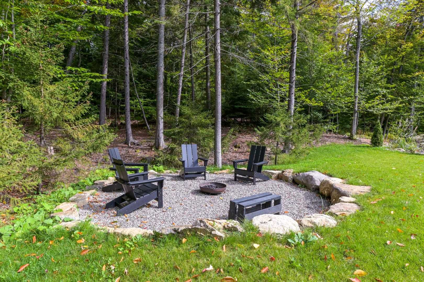 A yard includes a firepit area with seating and a stone surround.