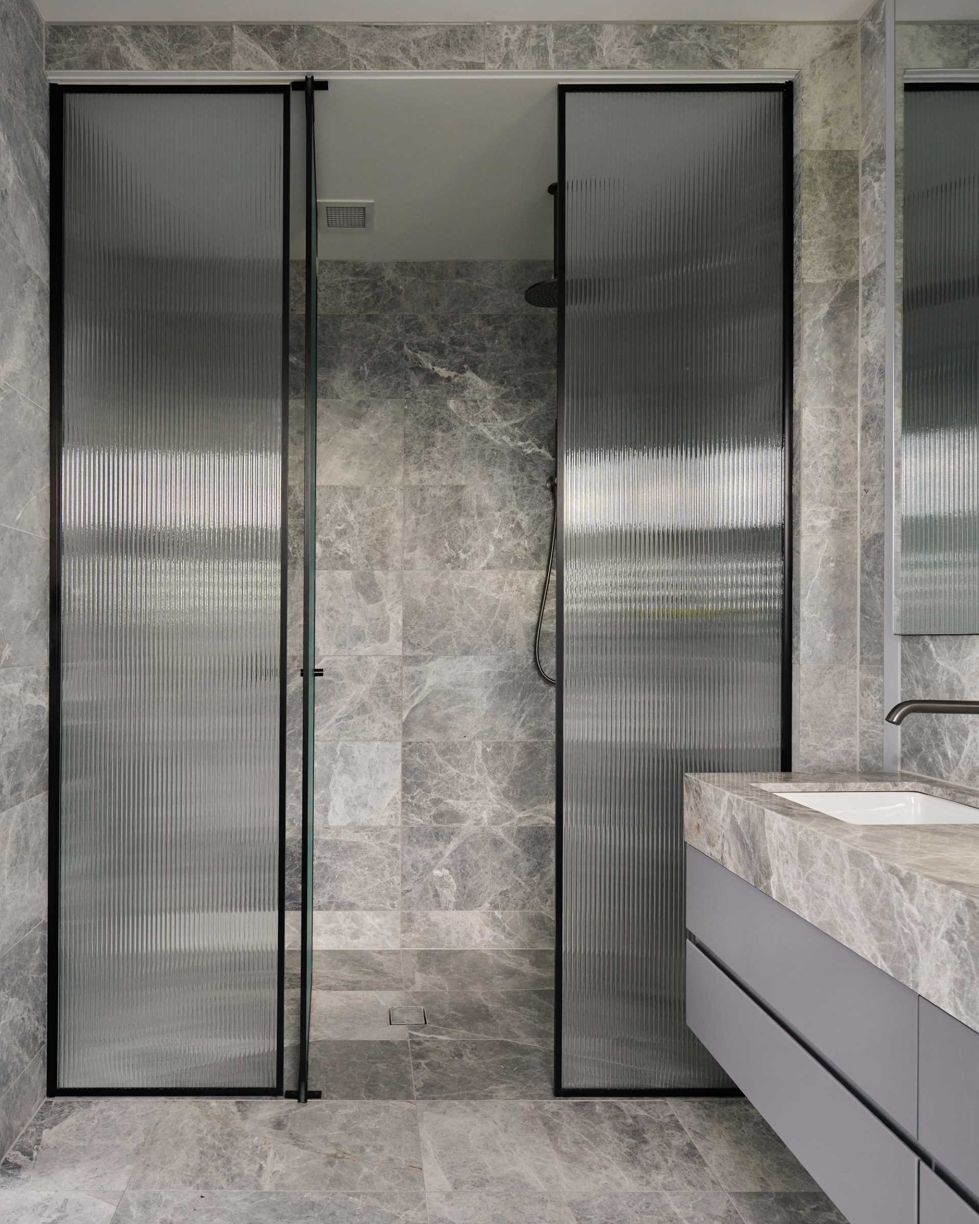 A walk-in shower with stone walls, a fluted glass screen, and black accents.