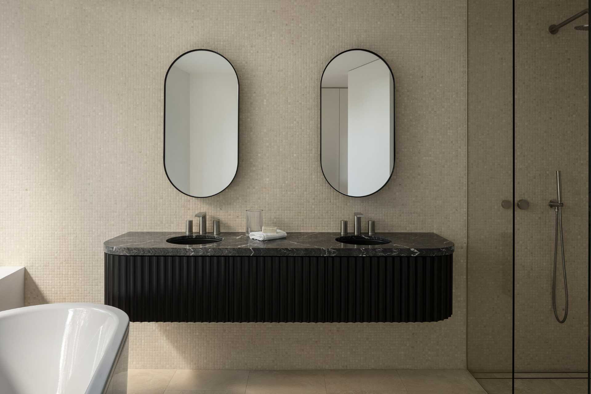 This modern bathroom is wrapped in a travertine mosaic tile providing a subtle textural quality to the space and contrasting with the solid floating vanity of stained timber and stone.