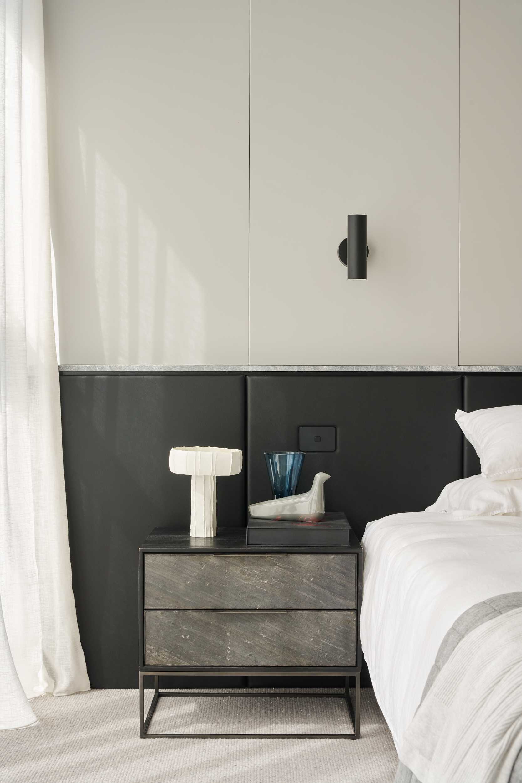 In this modern bedroom, a padded black headboard spans the room, while carpet is chosen flooring material.