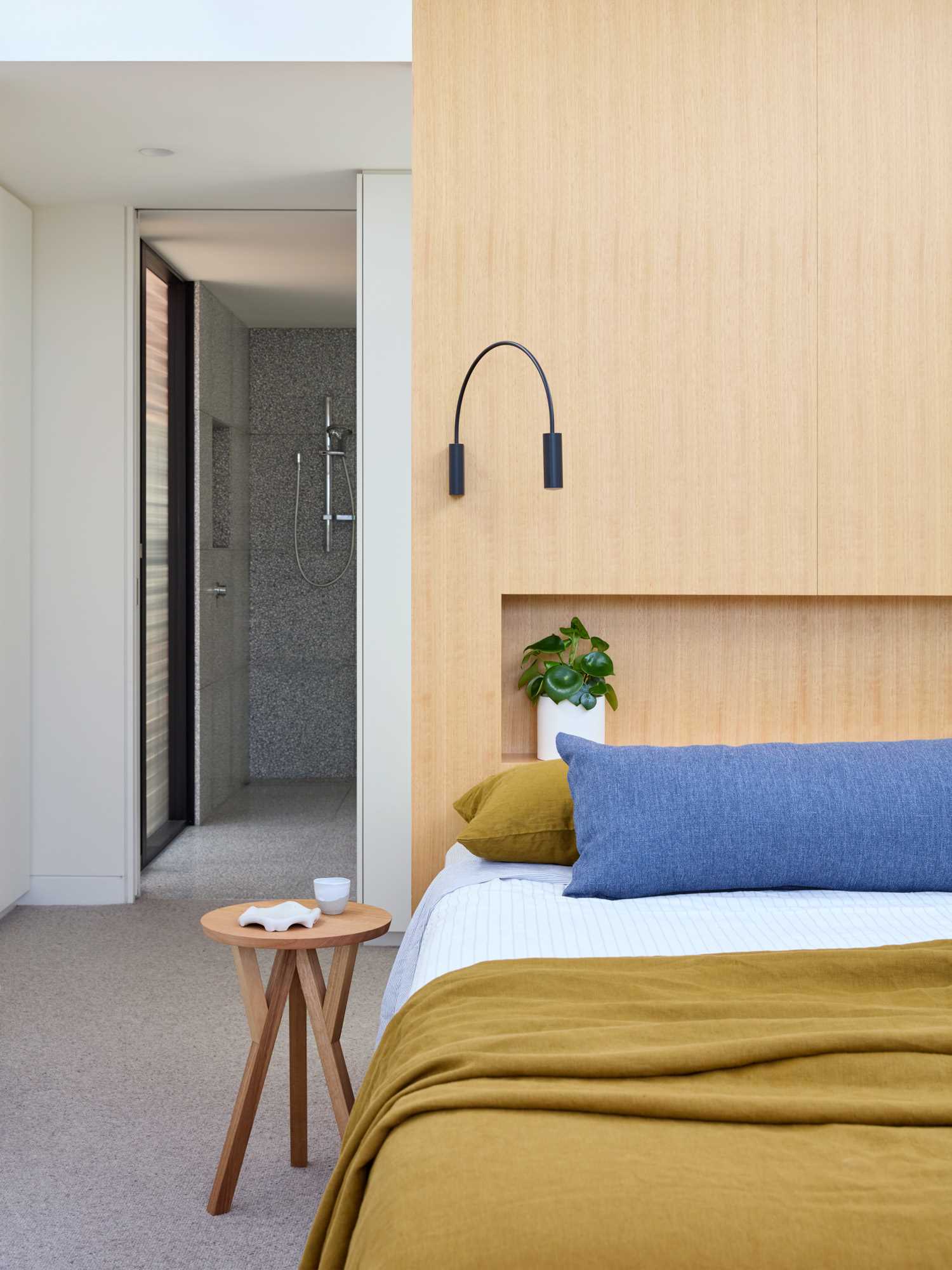 In this modern bedroom, a wood headboard has a built-in shelving niche and minimalist black sconces.