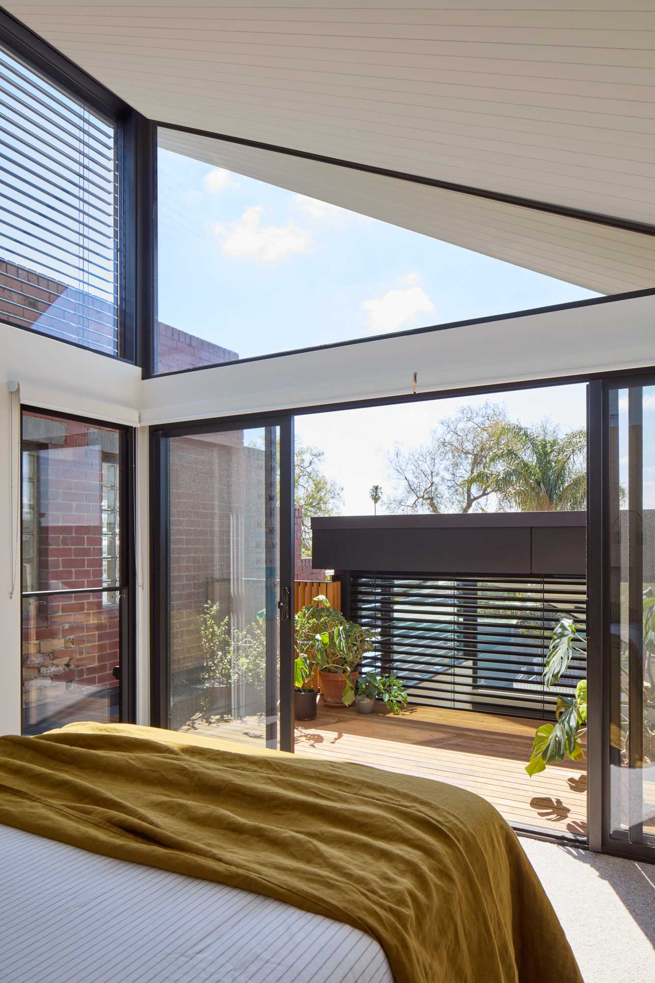 A modern bedroom with sliding glass doors that open to a private balcony with a variety of plants.