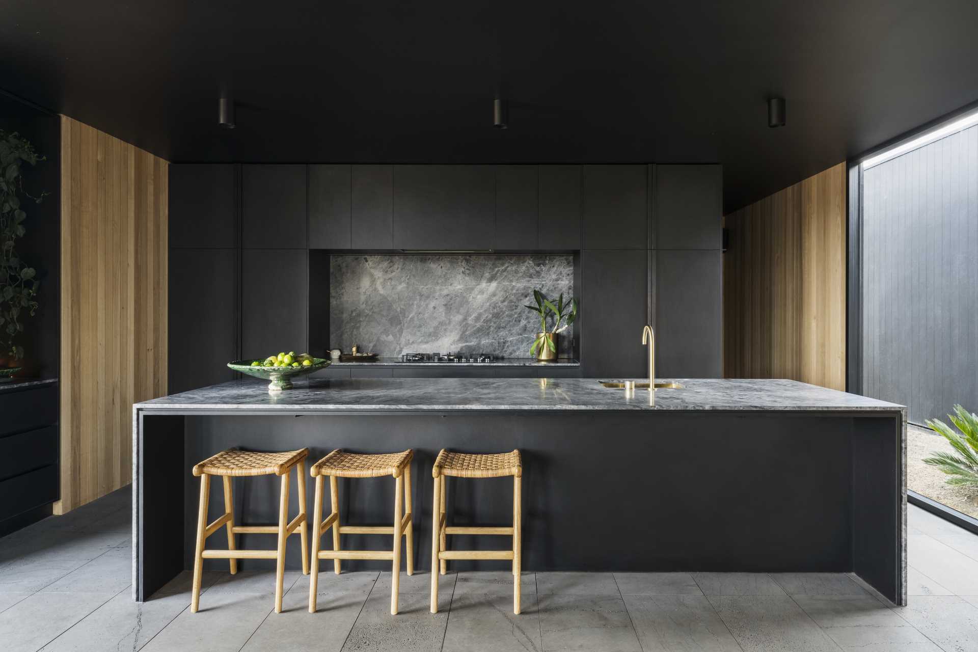 A modern black kitchen with minimalist cabinets, brass accents, and a long island.