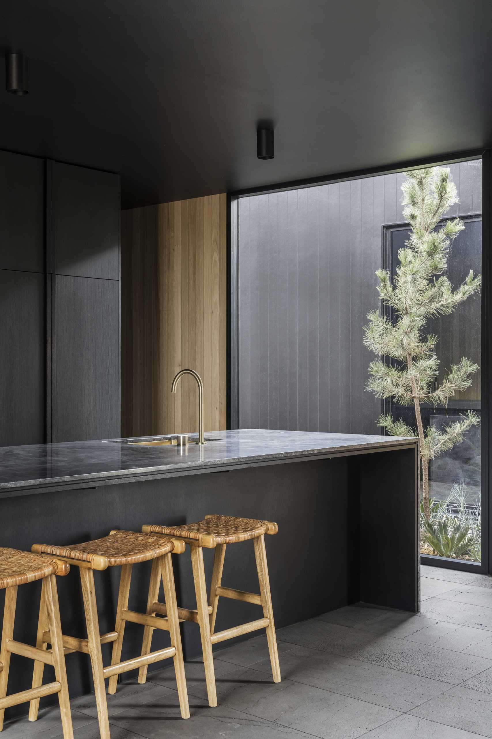 A modern black kitchen with minimalist cabinets, brass accents, and a long island.