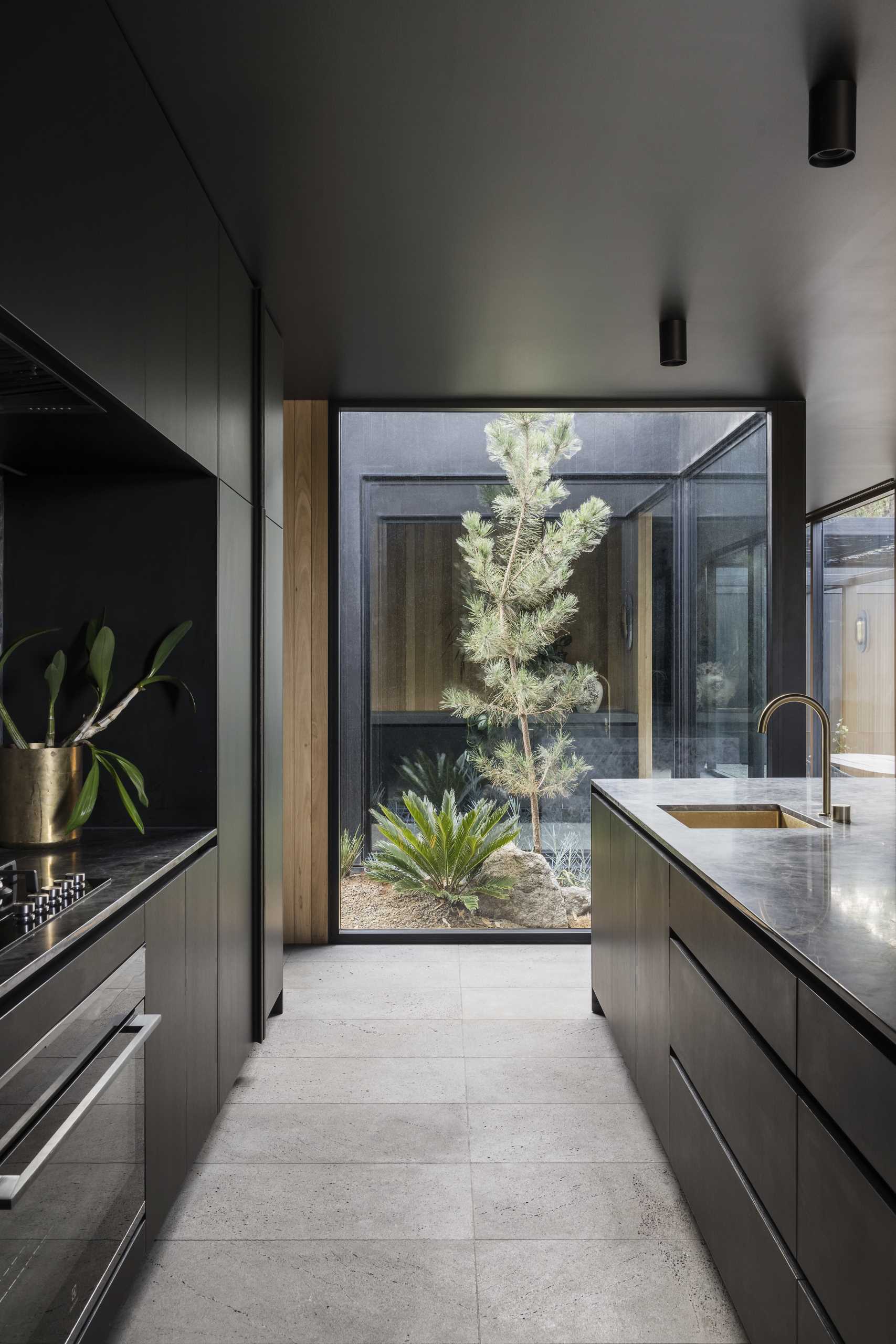 A modern kitchen with a full-wall window that provides a view of a small garden outside.