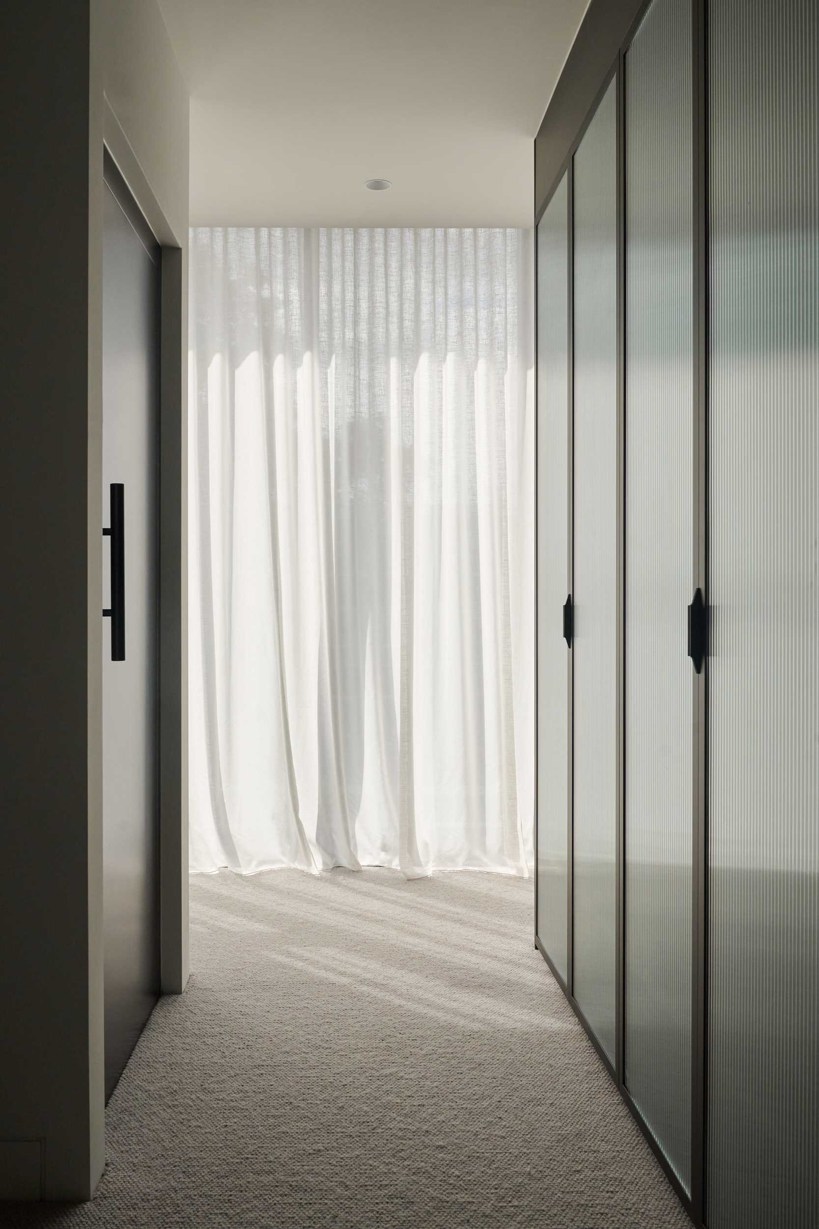A modern walk-through closet with fluted glass cabinet doors.