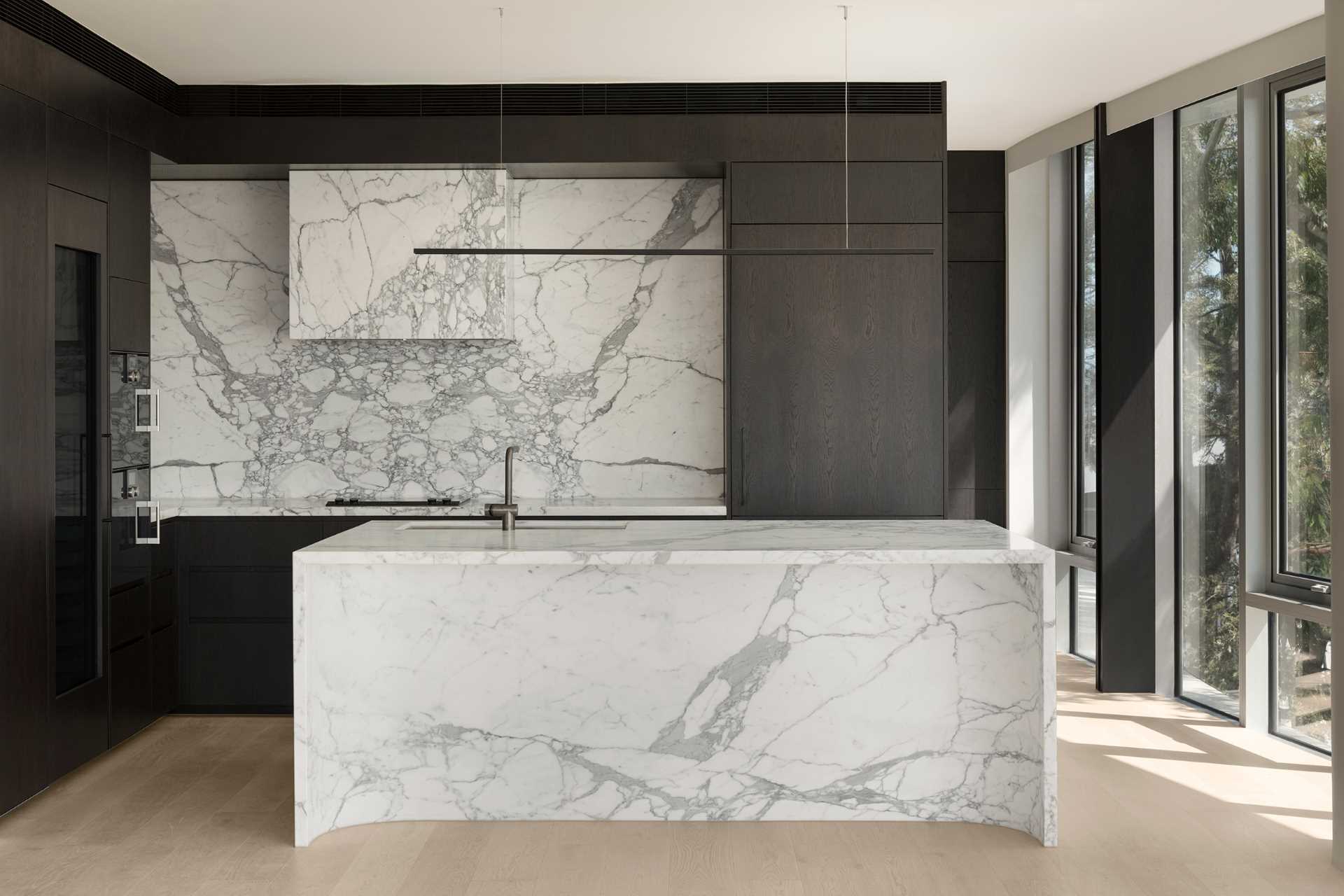 In this modern kitchen highly crafted joinery in natural timber and book-matched marble add to the overall feeling of warmth, contrast, and a refined approach to pared-down luxury.