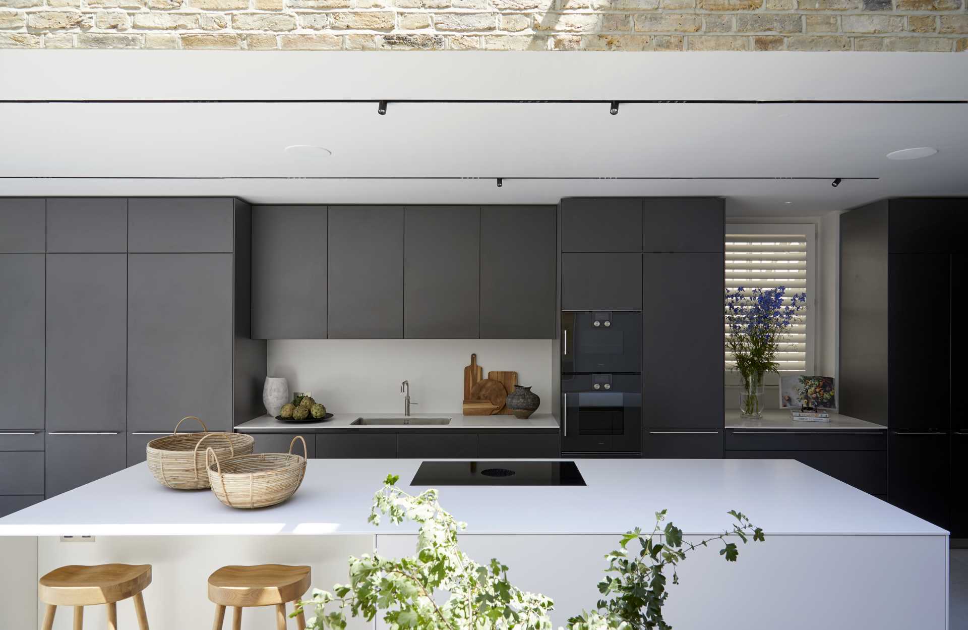 A modern kitchen with matte black cabinets, and a white backsplash and island.