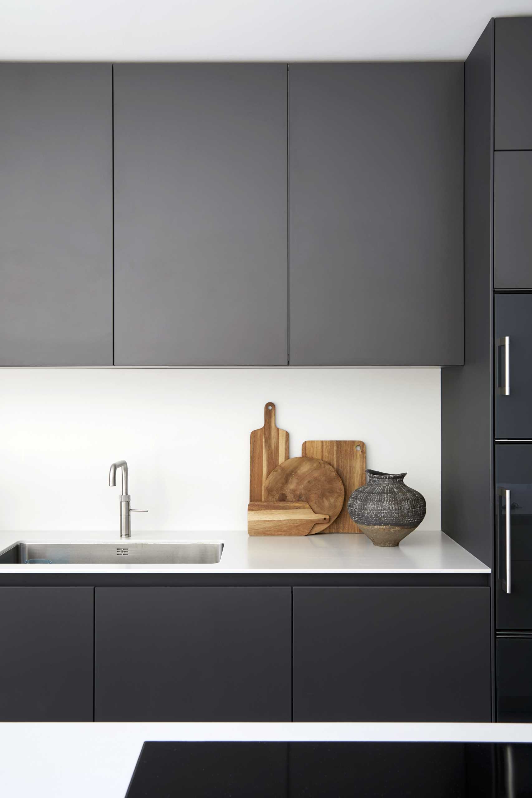A modern kitchen with matte black cabinets and white backsplash.