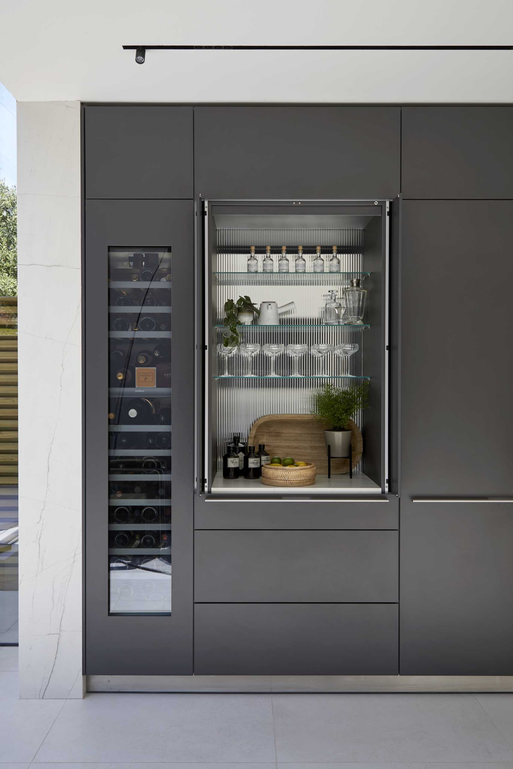 A modern kitchen cabinet hides a bar with glass shelves.