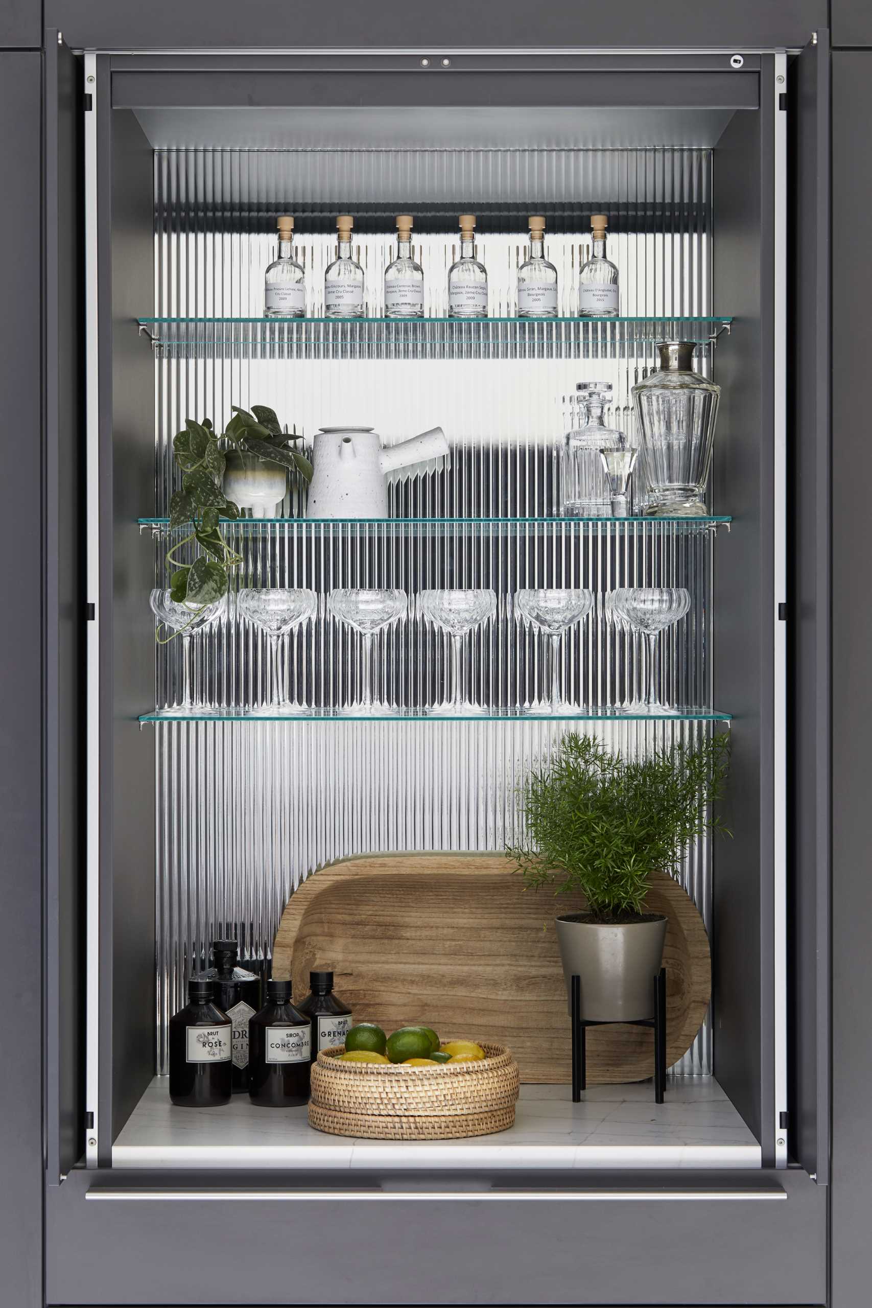 A modern kitchen cabinet hides a bar with glass shelves.