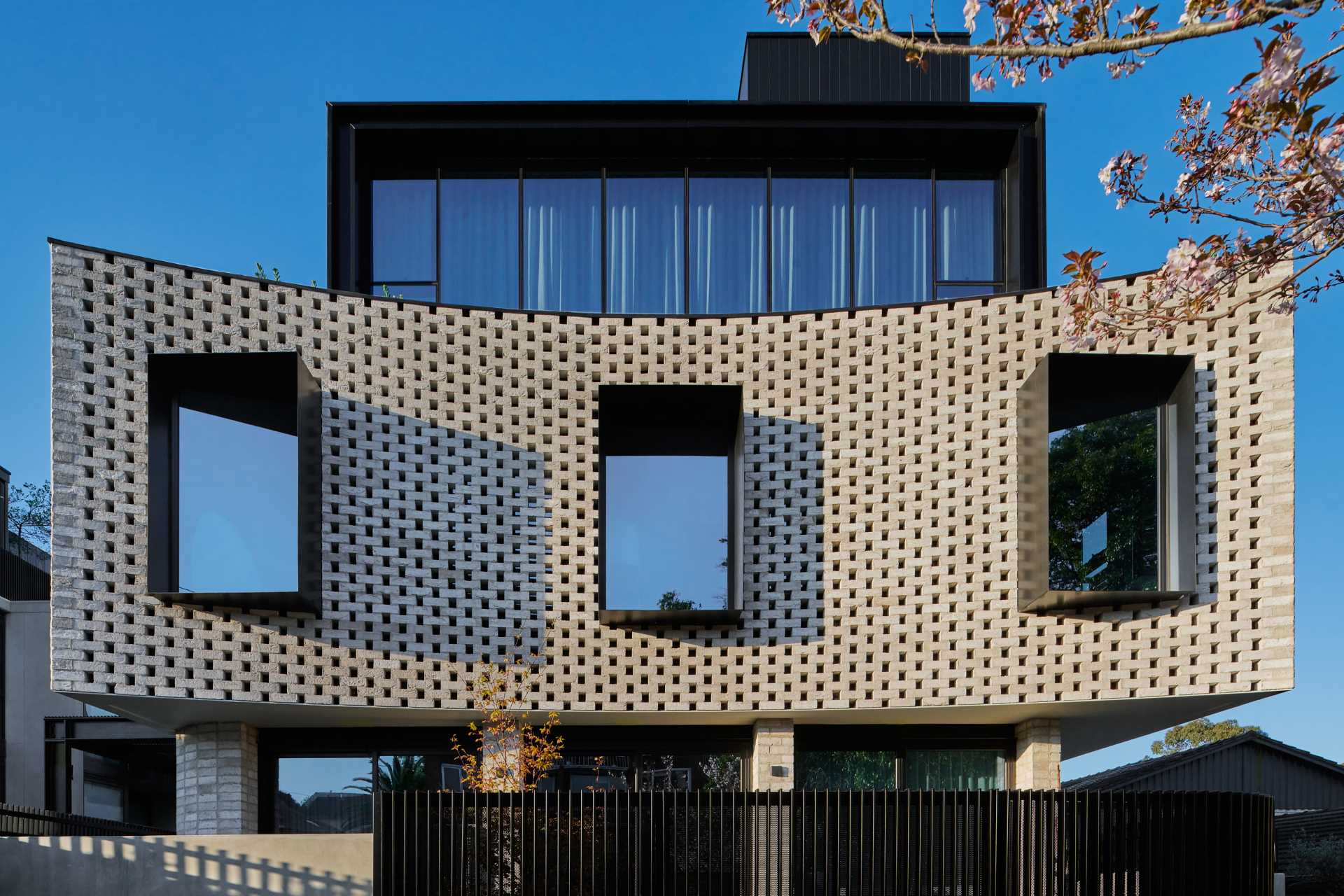 A curved brick facade with protruding black window frames that cast unique shadows.