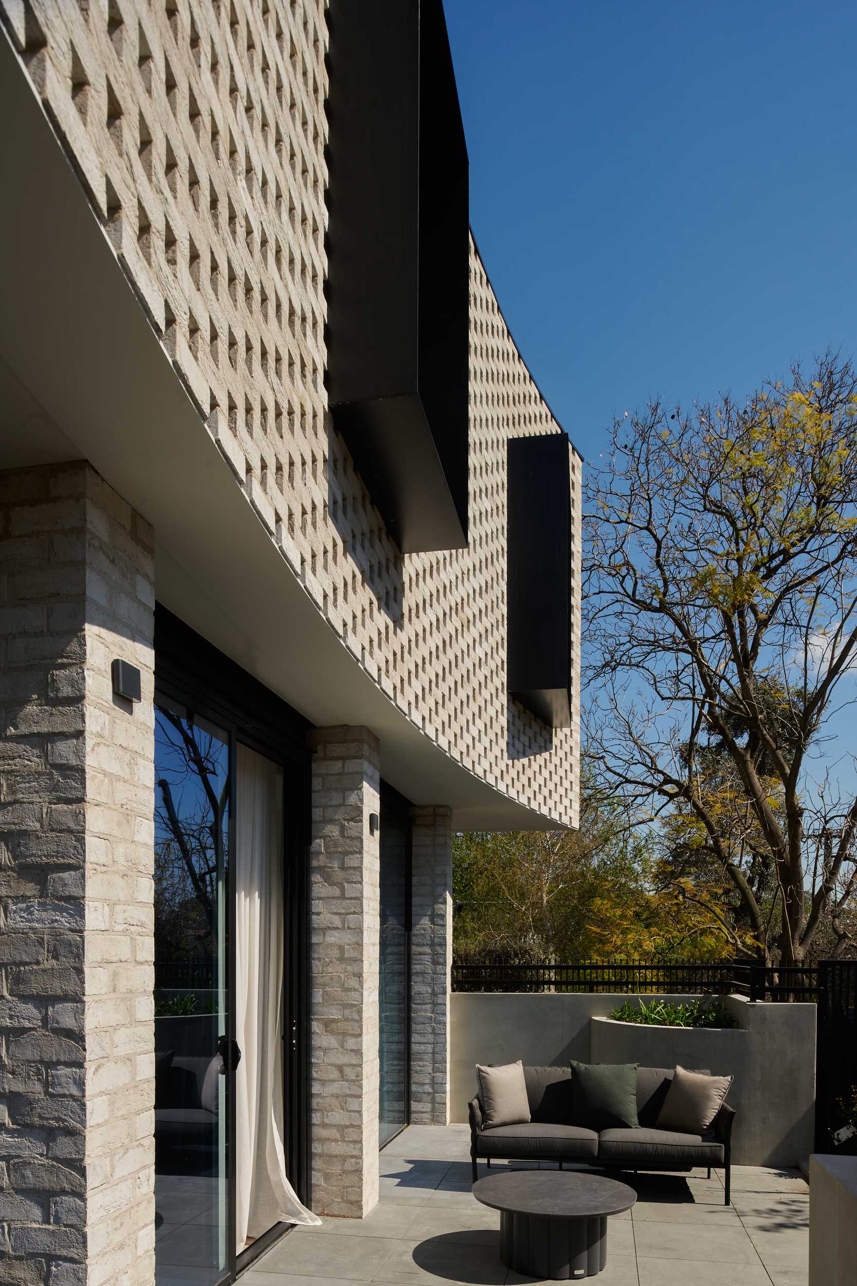 A curved brick facade with protruding black window frames and a patio below.